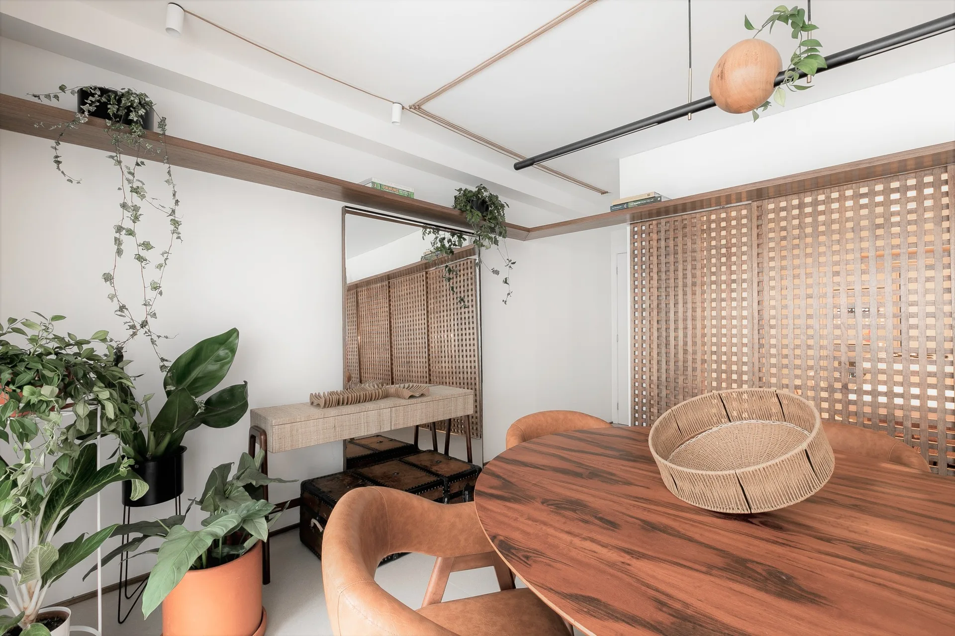 A modern dining area features a round wood table, curved tan chairs, a wooden lattice screen partition, and potted green plants.