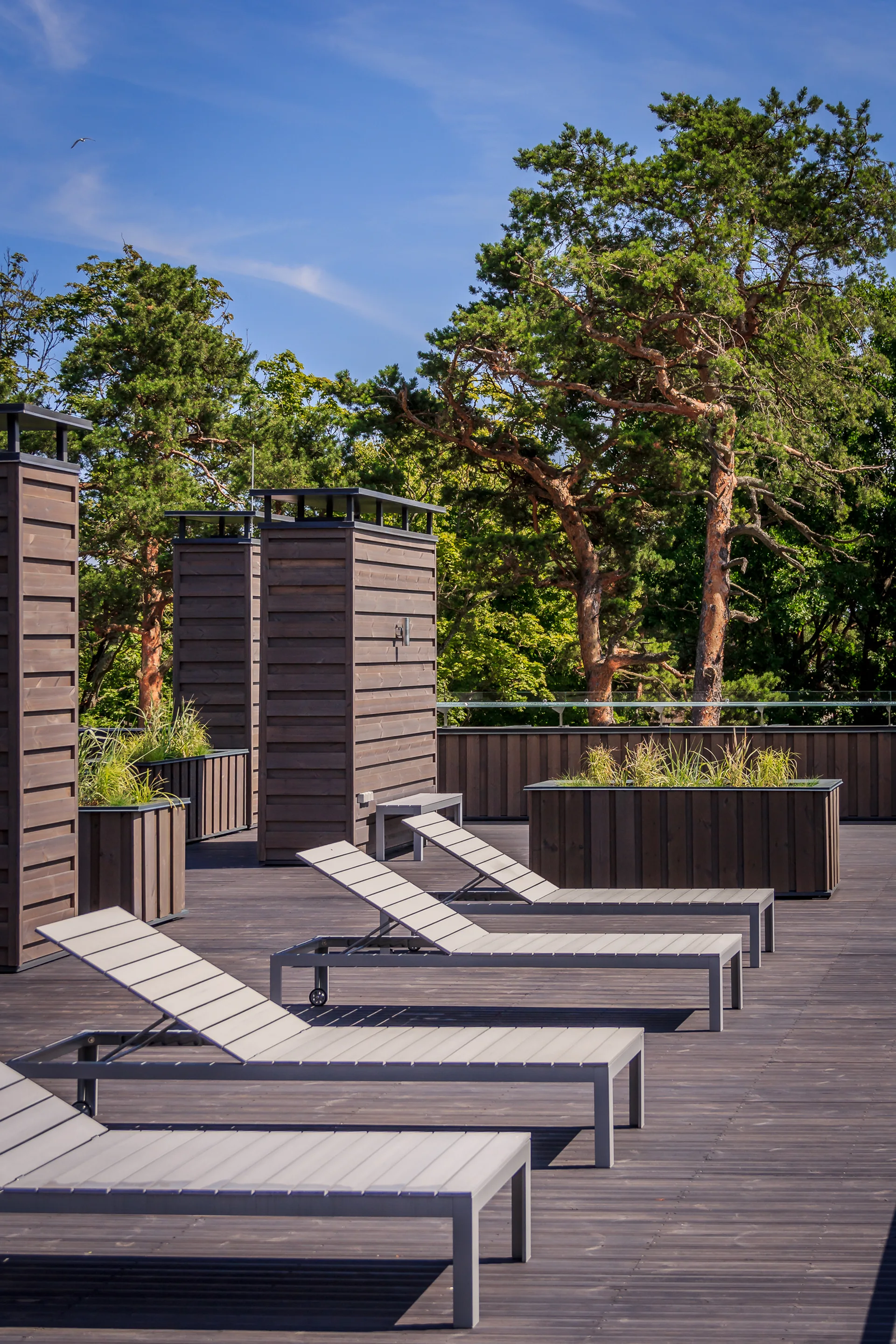 Multiple grey slatted chaise lounges sit on a dark wood terrace deck next to wood-paneled privacy screens and planter boxes.