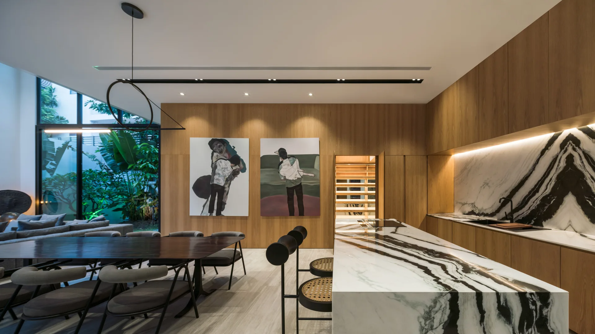 A modern open-concept kitchen features a large veined marble island, wood-paneled walls with two art pieces, and an adjacent dark wood dining table.
