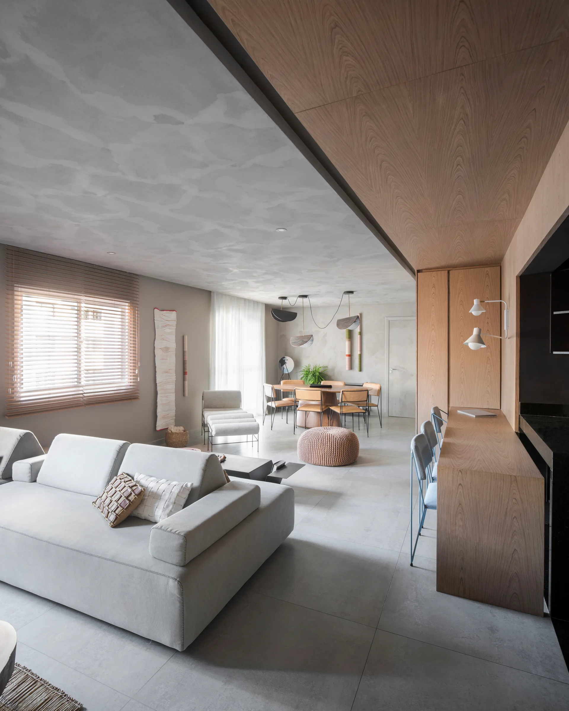 A modern open-plan living and dining room features a grey sectional sofa, a textured plaster ceiling, and warm wood-toned paneling and cabinetry.