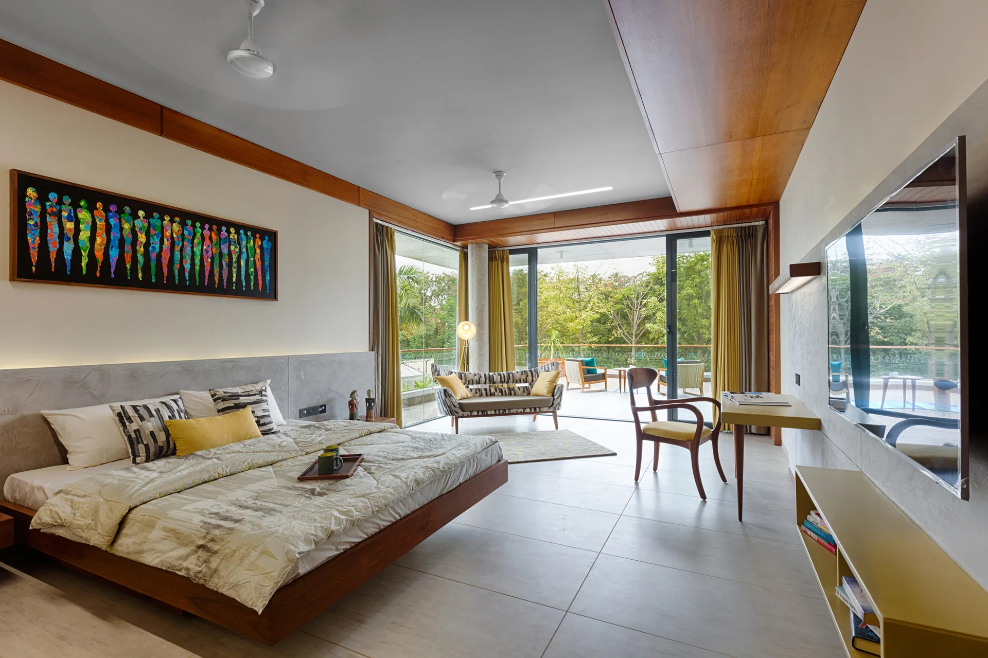 A modern bedroom featuring a wooden platform bed, plaster-finish wall, minimalist desk, and sliding glass doors leading to a tree-lined balcony.
