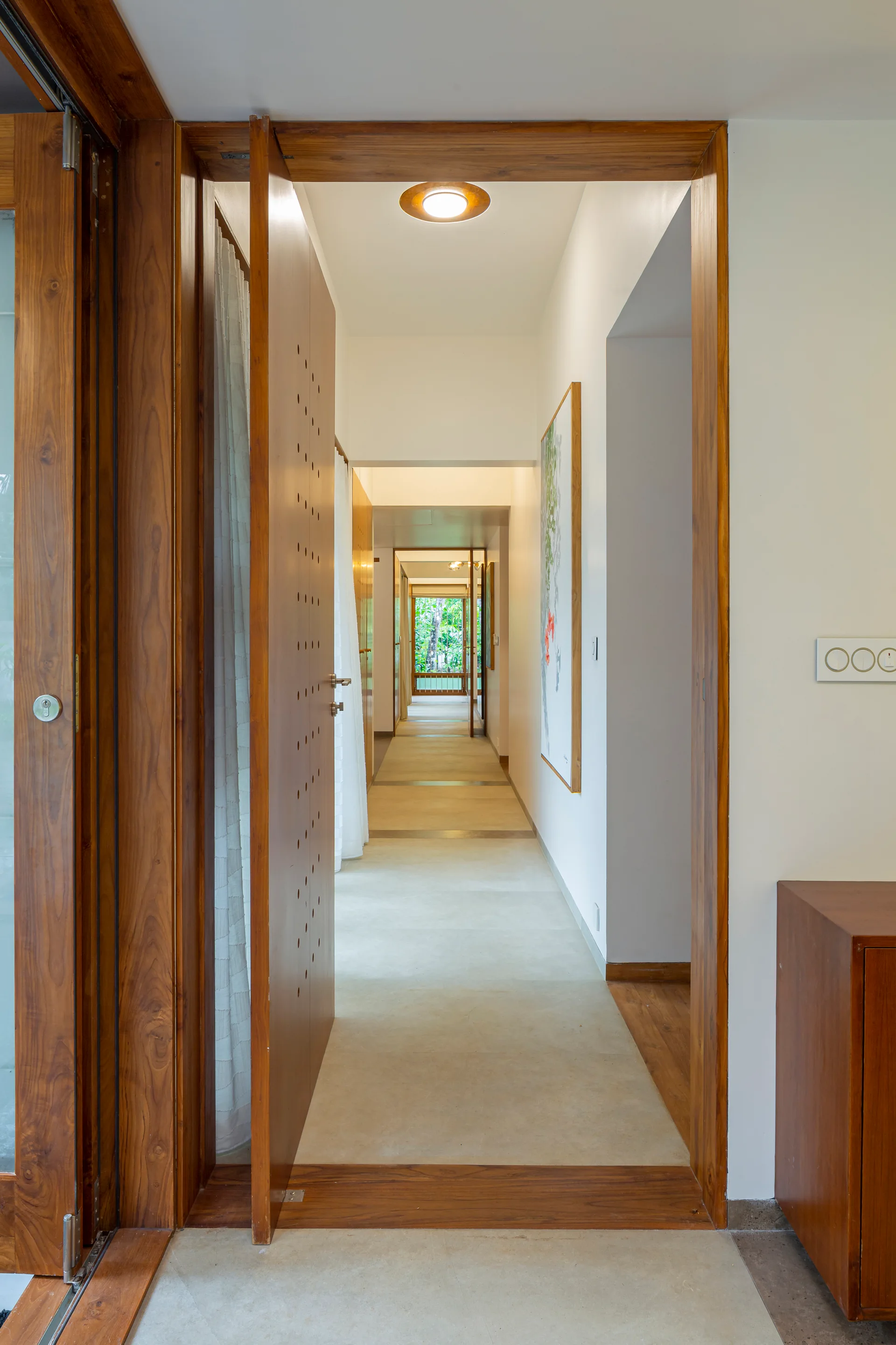 A long minimalist residential hallway featuring clean white walls, smooth beige flooring, and rich natural wood door frames.