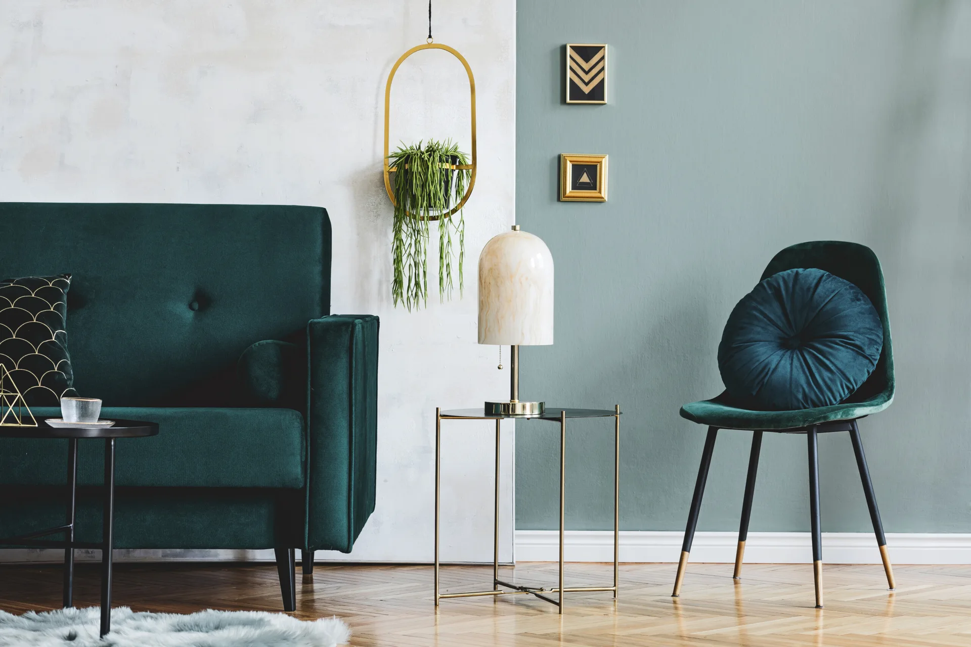 An emerald green velvet sofa and matching chair sit on herringbone wood floors against a two-tone sage green and white wall.