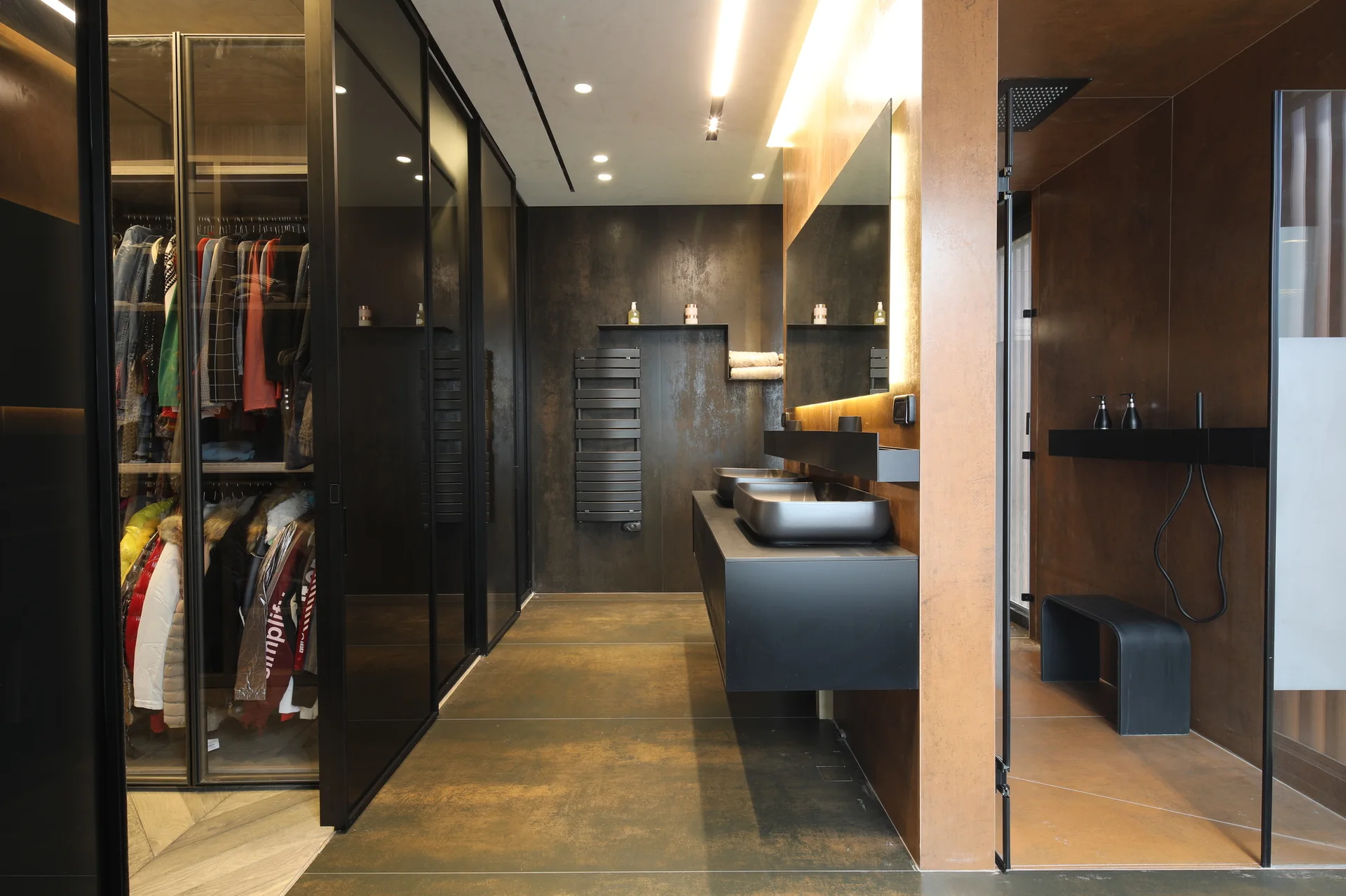 A modern bathroom with copper metallic walls features a floating black double vanity next to glass-fronted closet doors and a walk-in shower.