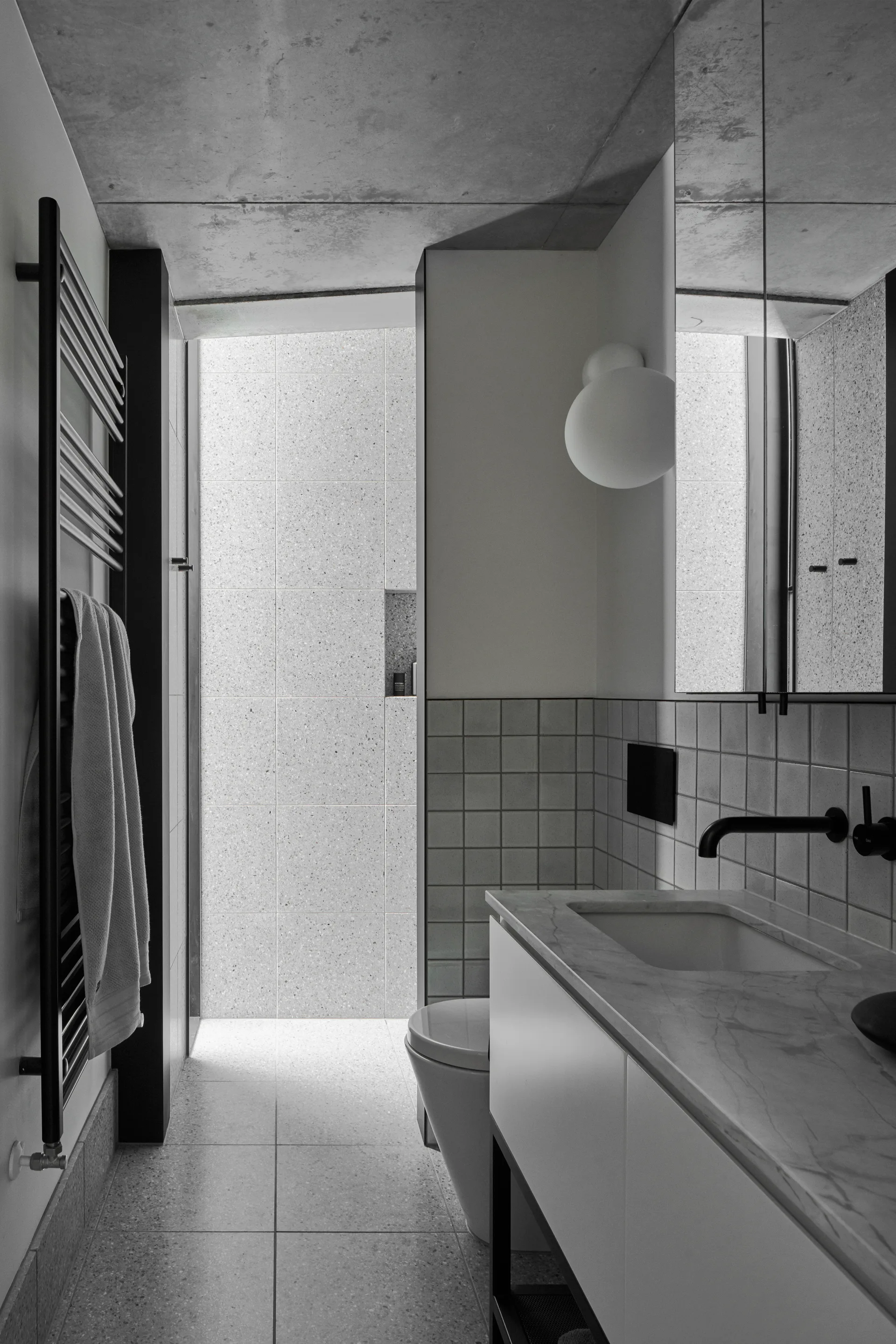 A modern narrow bathroom featuring a raw concrete ceiling, a white floating vanity with a marble countertop, and gray terrazzo tile floors.