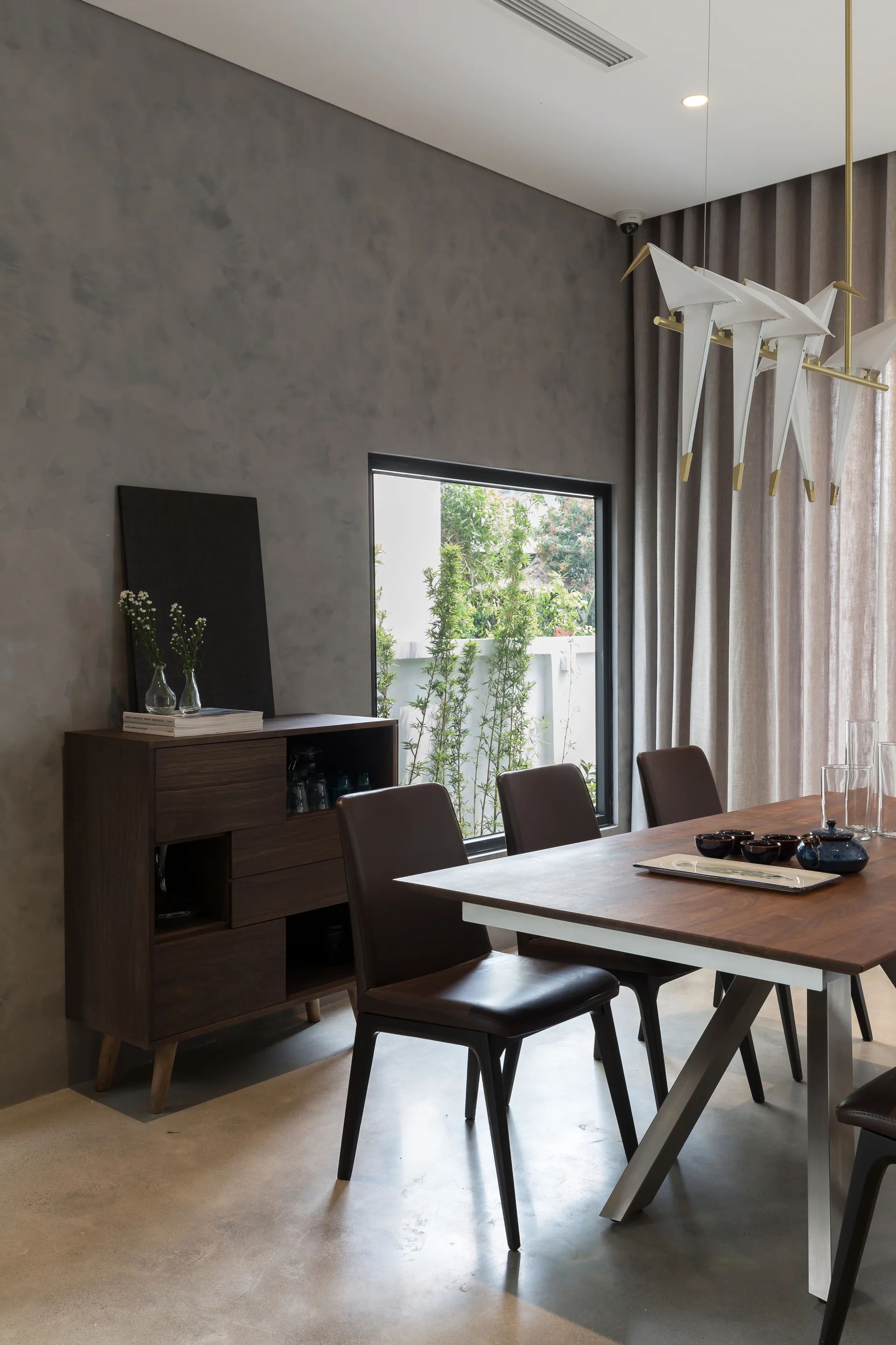 A modern dining room with a dark wood table, brown leather chairs, textured grey plaster walls, and a white sculptural bird chandelier.