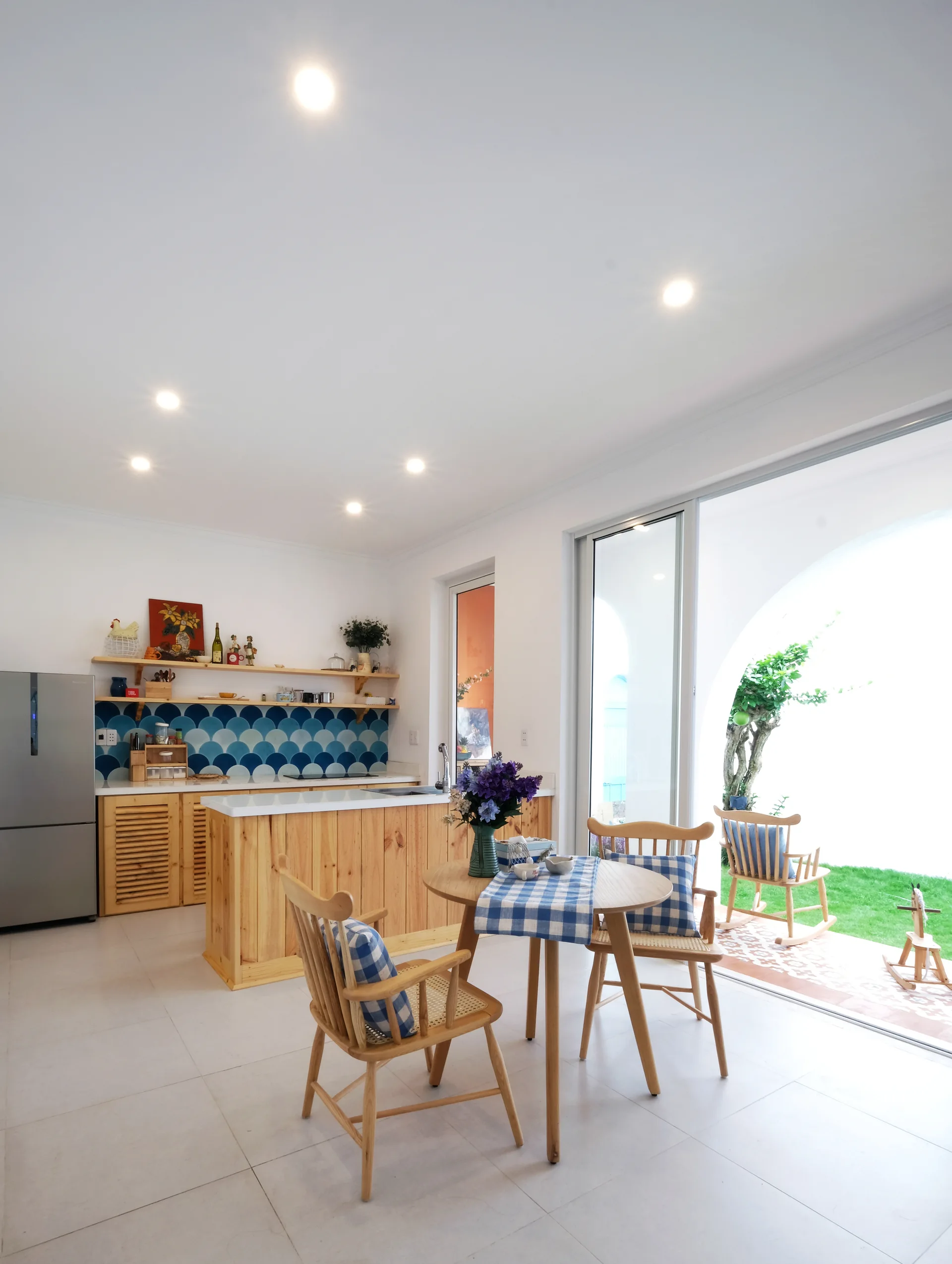 A bright kitchen features a blue scalloped tile backsplash, a wooden island, and a dining table next to sliding doors opening to a grassy patio.