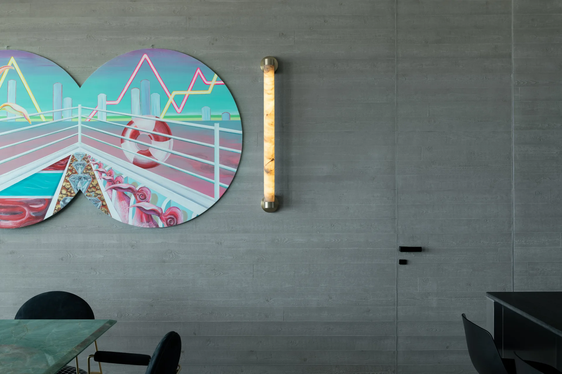 A textured grey wood-grain paneled wall features an illuminated stone wall sconce, a colorful circular painting, and a flush integrated door.