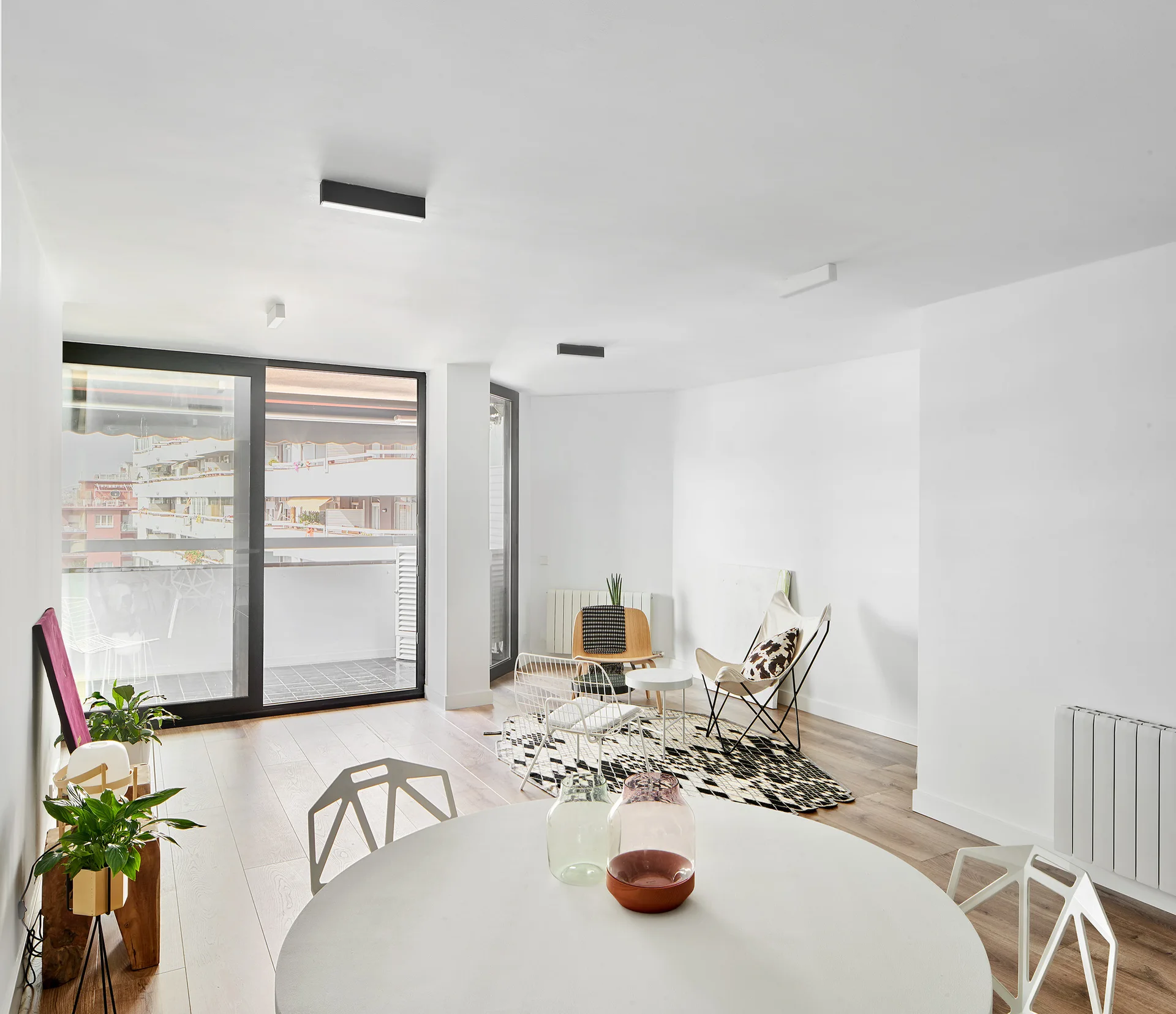 A minimalist open-plan living and dining area with a round white dining table in the foreground and a geometric rug in the background.