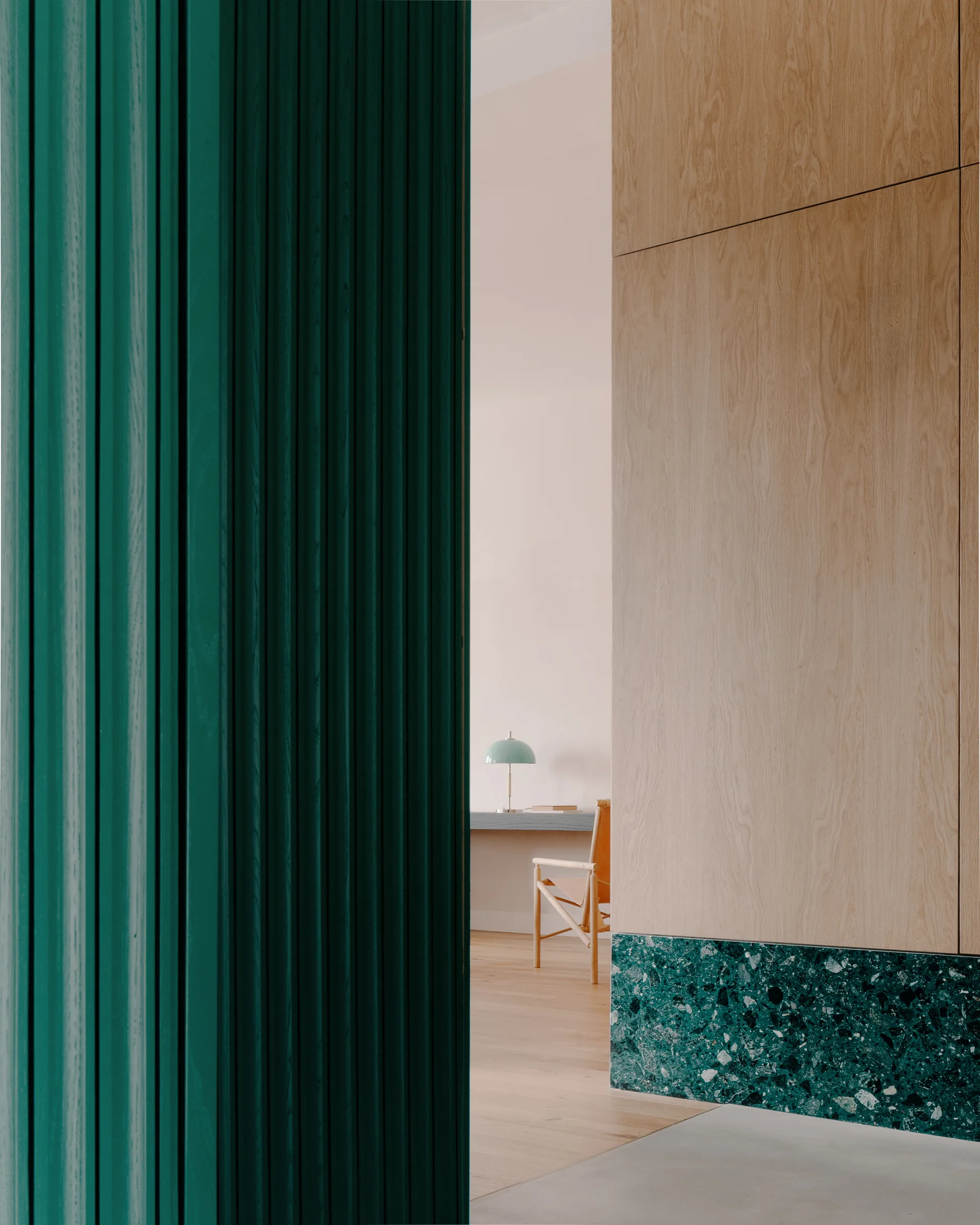 An interior corridor features a dark green fluted wall, light wood paneling with a green terrazzo base, and a desk visible in the background.
