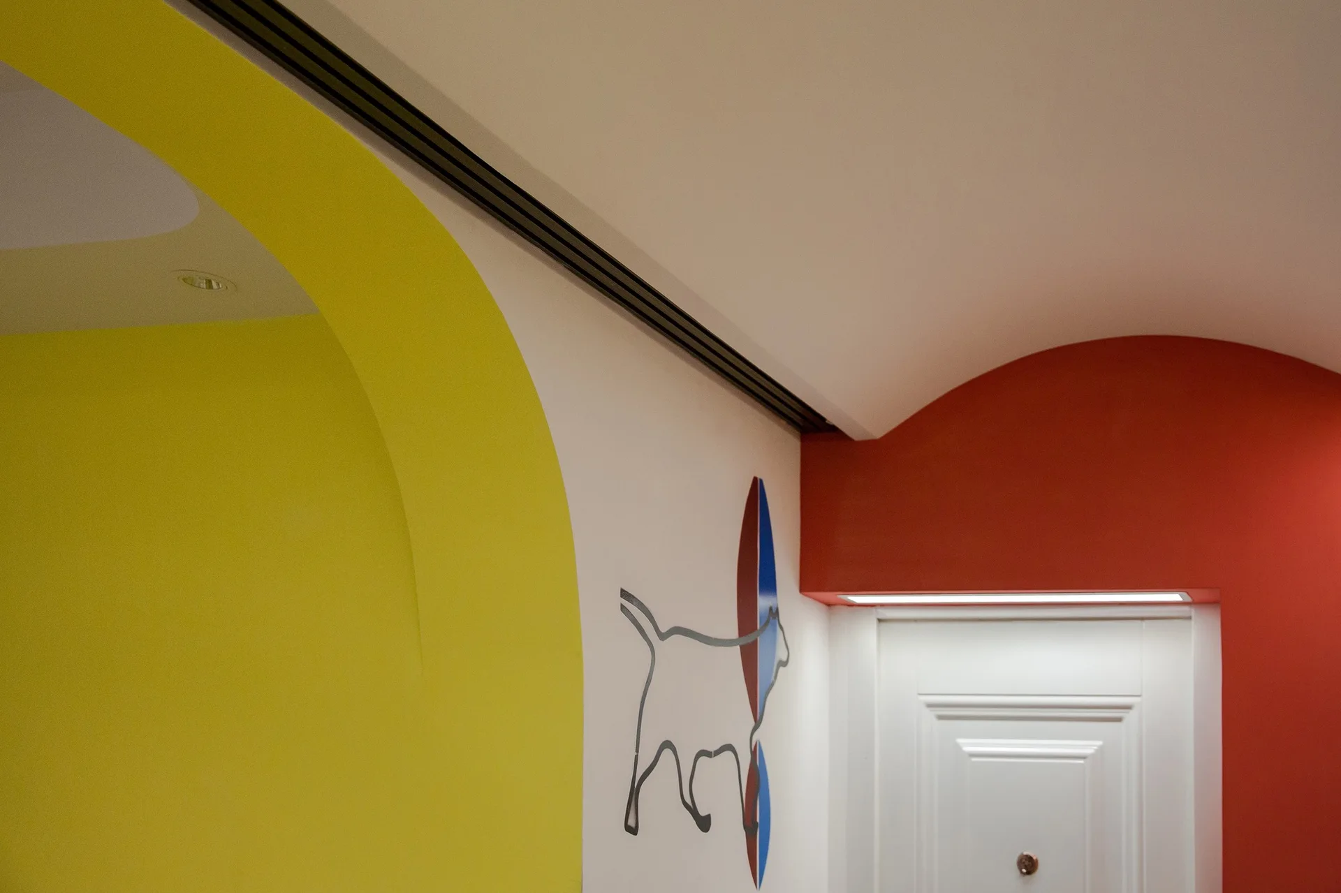 A bright yellow curved archway and a red accent wall frame a white paneled doorway decorated with a dog graphic.