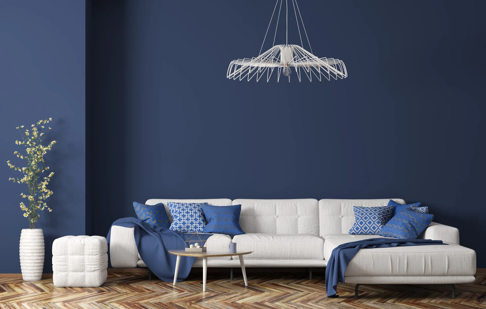 A white sectional sofa sits against a navy blue wall in a living room with herringbone wood flooring and a wire pendant light.