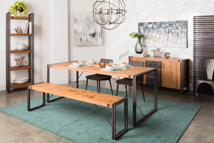 A modern dining room features a wood and metal dining table with a matching bench and grey chairs on a teal rug.