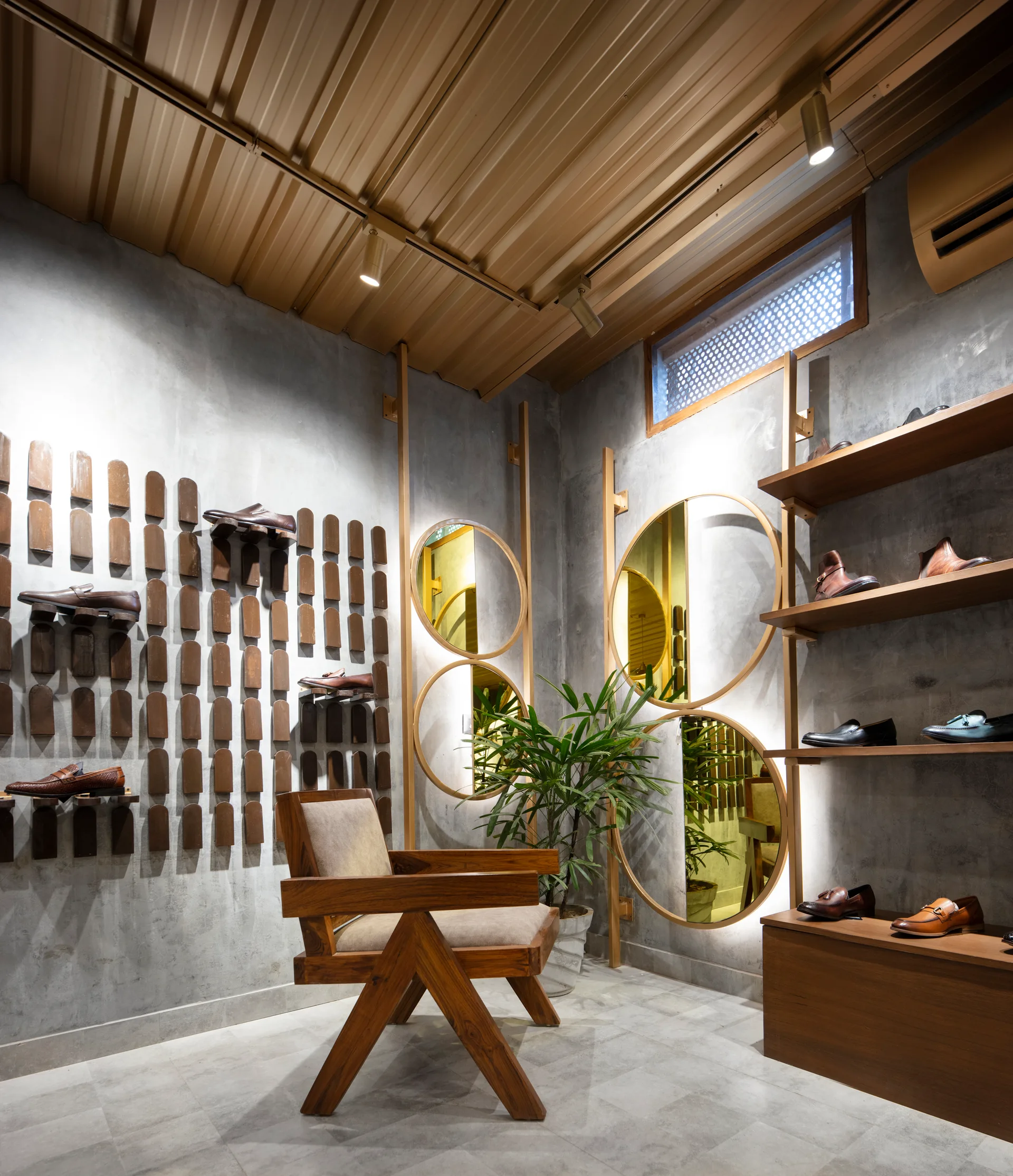 An industrial showroom features concrete walls, wooden shelves displaying shoes, a wood armchair, and large circular backlit mirrors.
