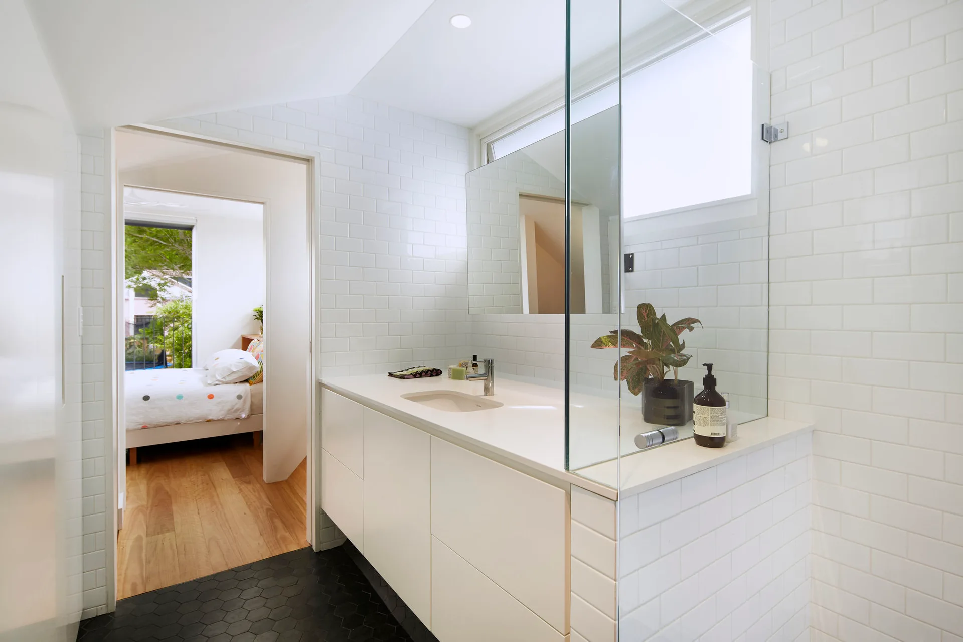 A modern bathroom with white subway tile walls, a minimalist white vanity with an integrated sink, and black hexagonal floor tiles.