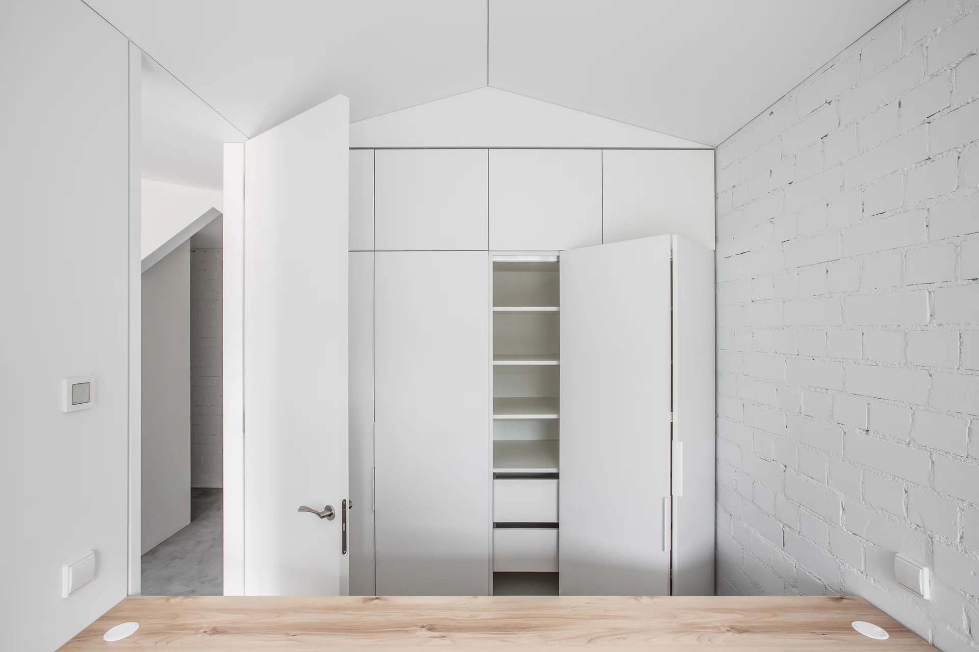 A minimalist room features white built-in storage cabinetry next to a painted brick wall, with a light wood tabletop in the foreground.