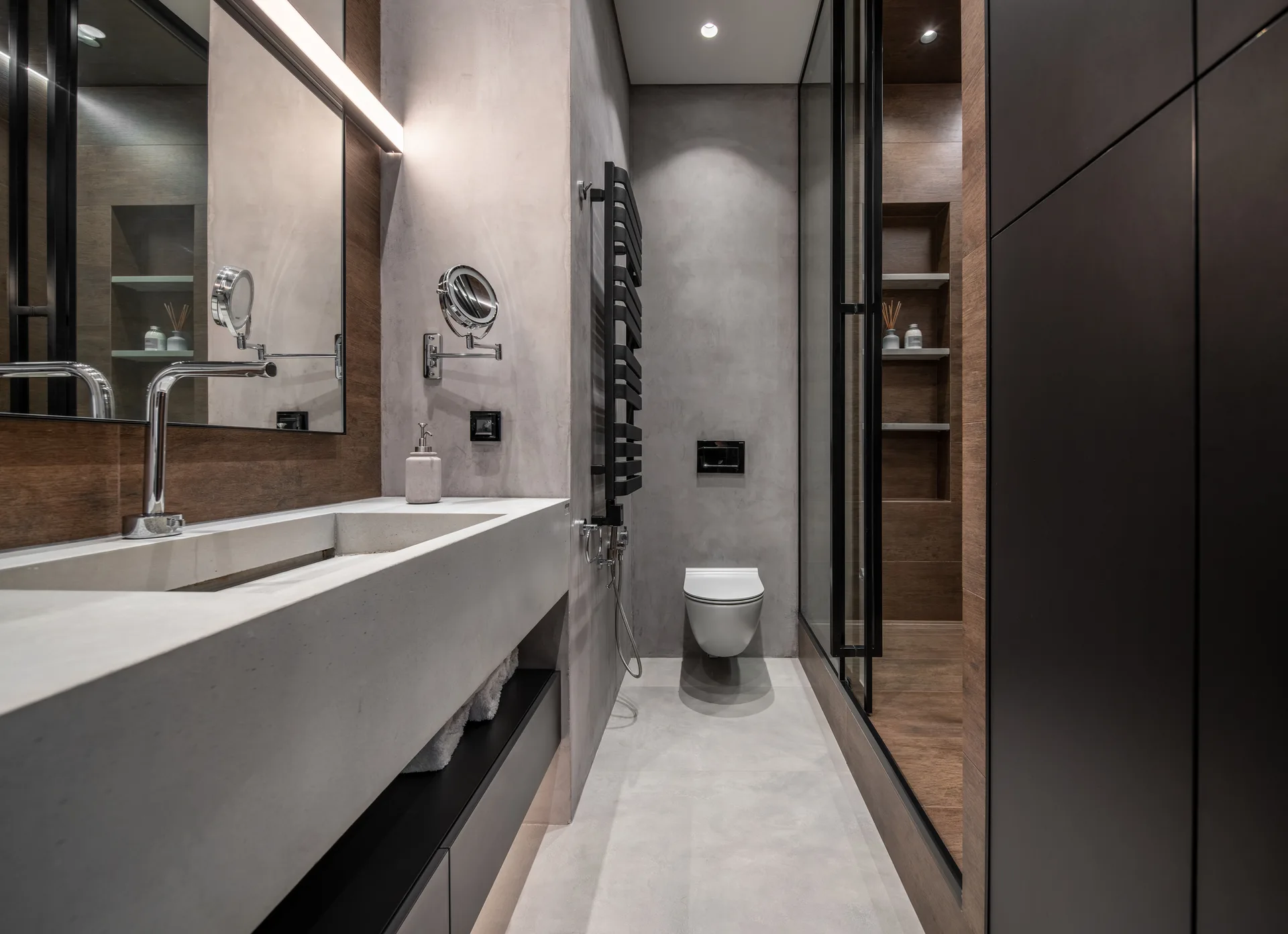 A modern bathroom features a concrete floating vanity, a wall-mounted toilet, and a glass-enclosed shower accented by warm wood paneling.