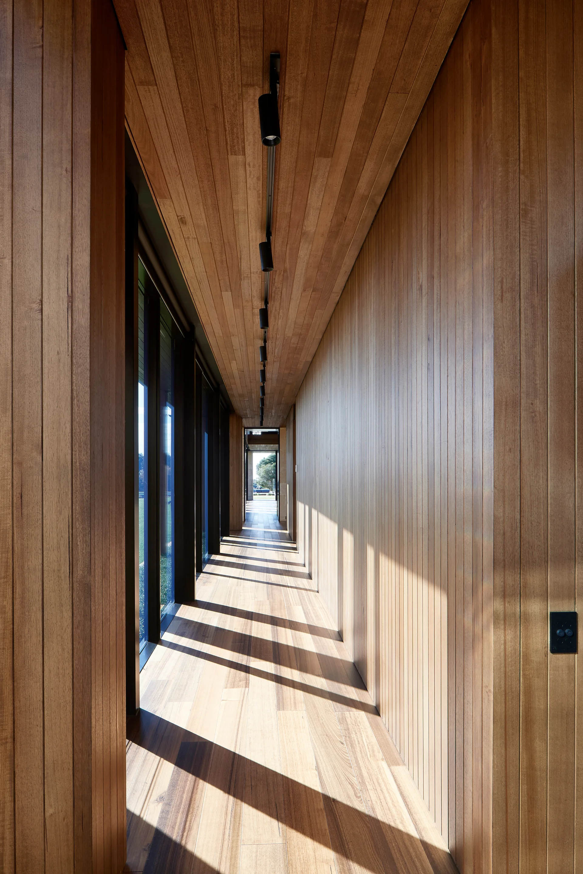 A minimalist hallway lined with vertical wood slat walls, matching wooden ceilings and floors, and a black track light system.