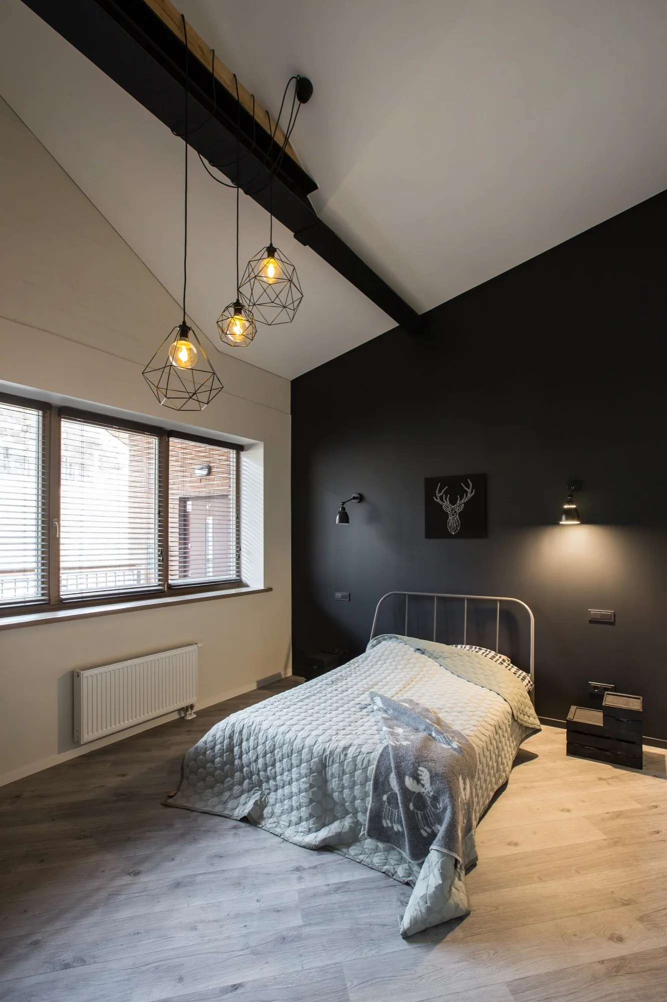 A modern bedroom features a metal bed against a black accent wall, geometric pendant lights, and a sloped ceiling with an exposed beam.