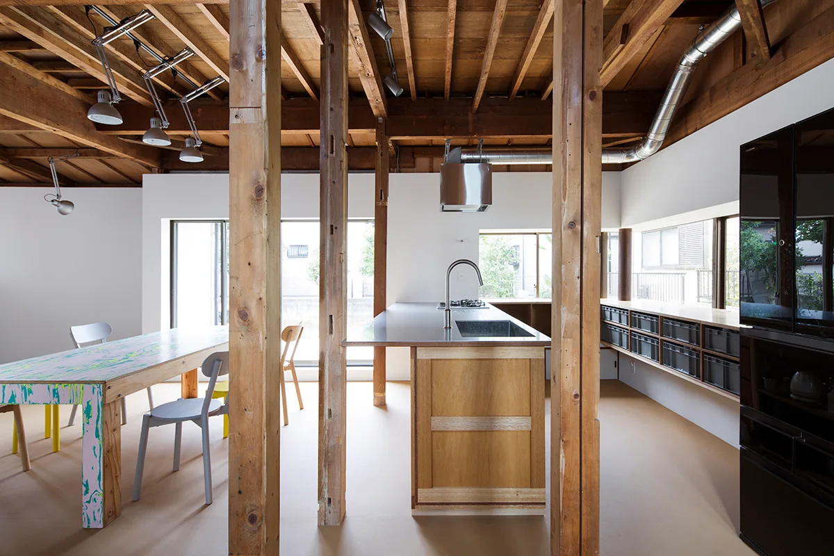 An open-concept kitchen features a wooden island with a stainless steel countertop, exposed timber ceiling beams, and a colorful marbled dining table.