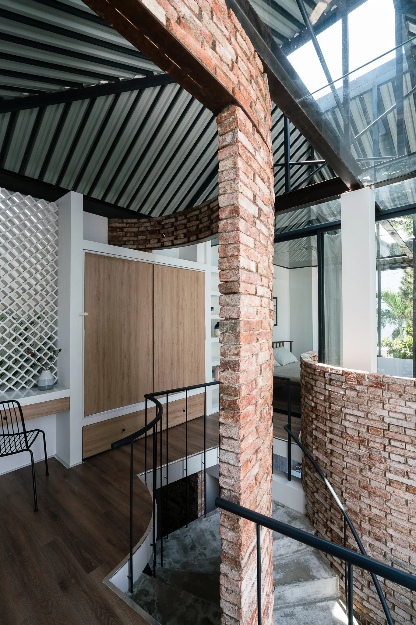 An interior staircase featuring an exposed brick column, modern black metal railings, wood-toned built-in cabinets, and a glass skylight.