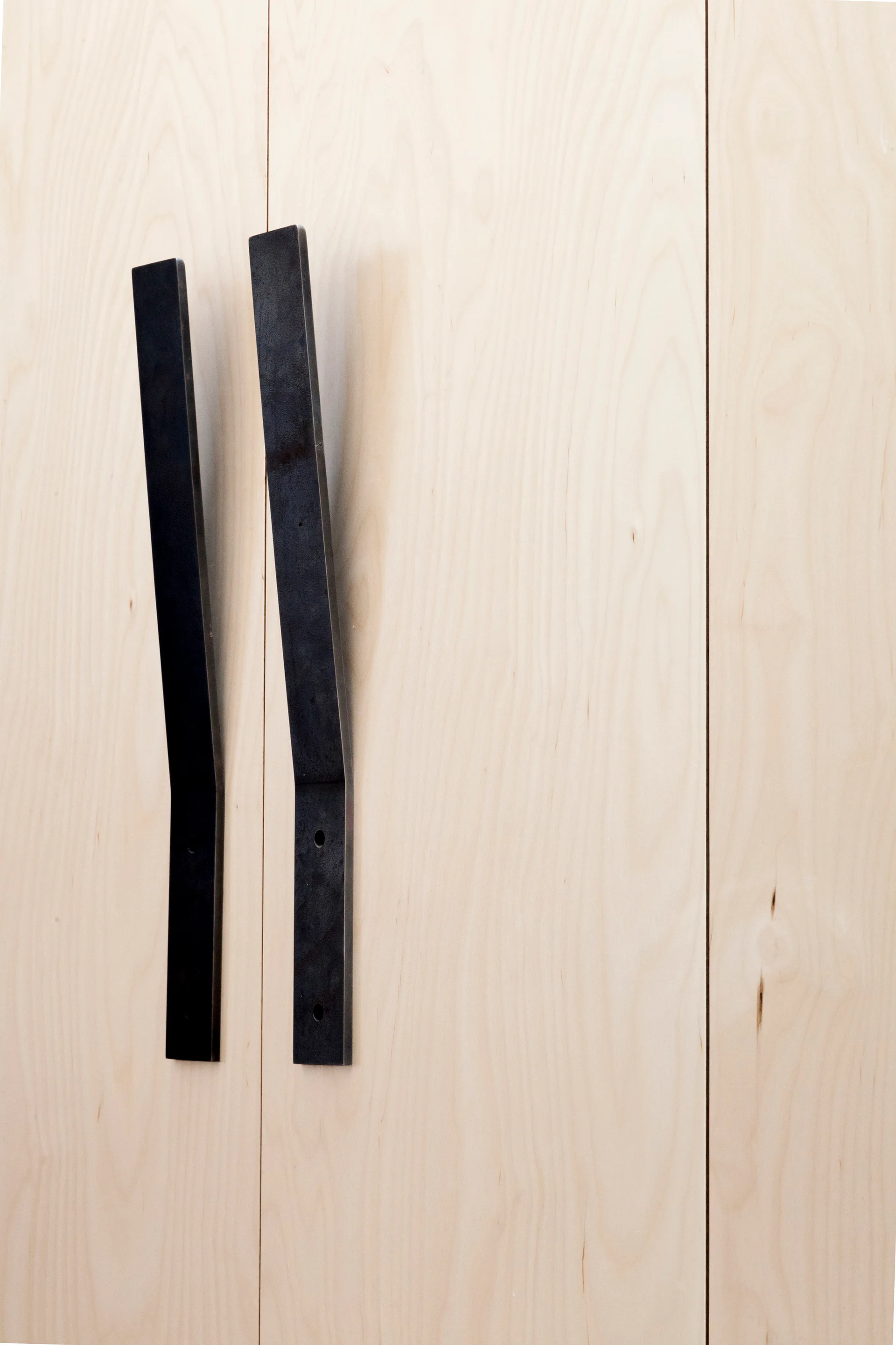 A close-up shot of two long matte black metal bar handles mounted vertically on light-colored wood cabinet doors.
