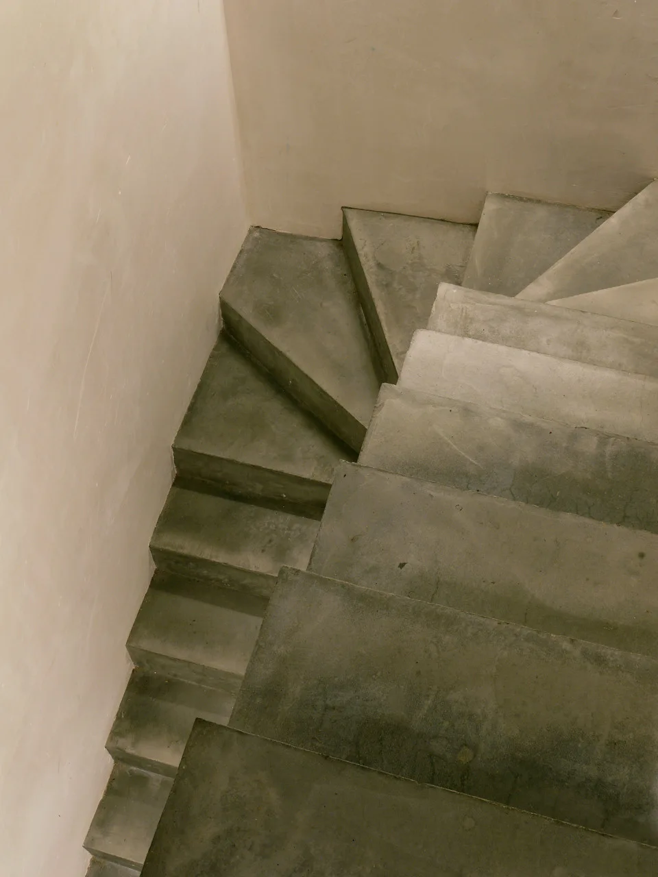 An overhead view of a minimalist concrete staircase winding alongside a smooth beige plaster wall.