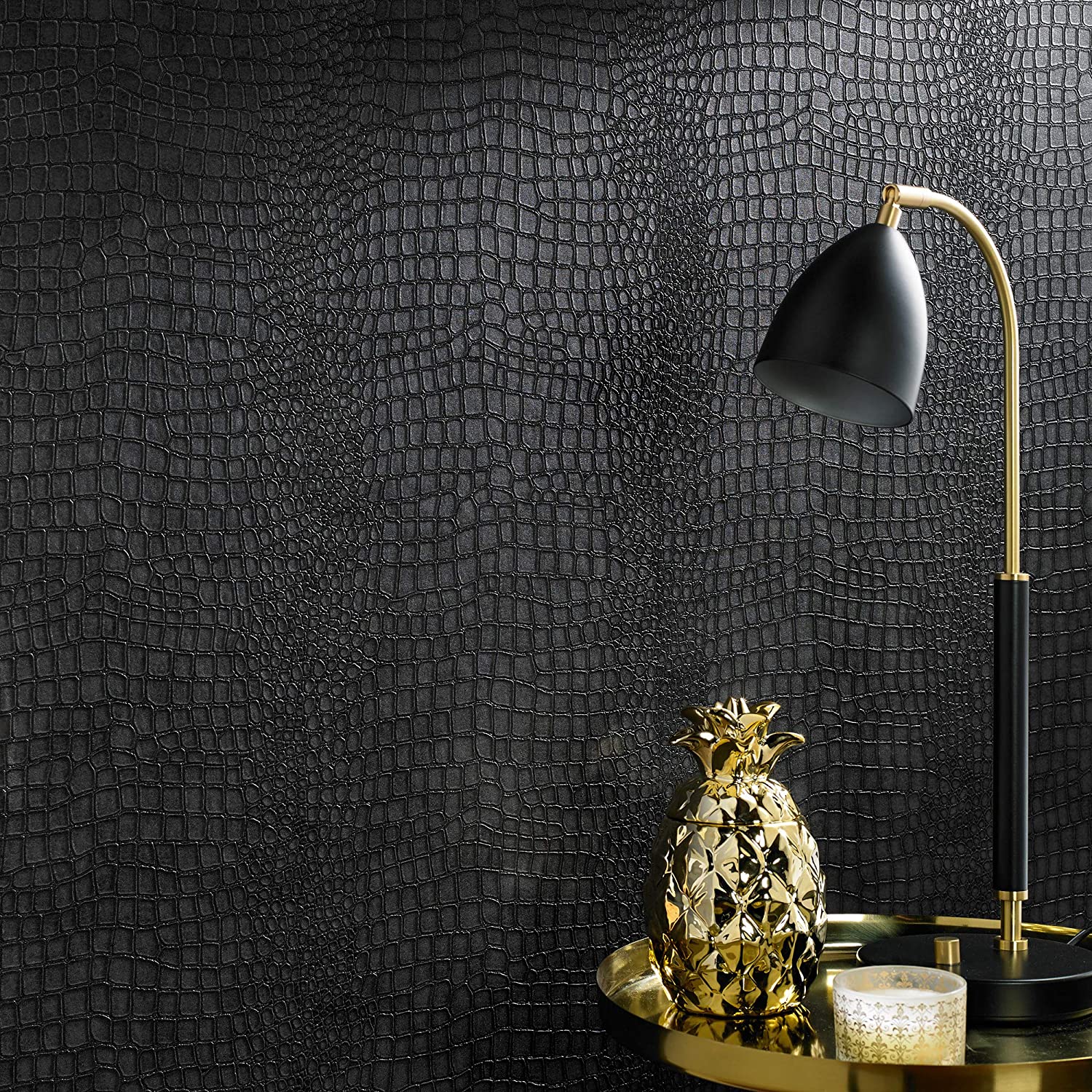 A close-up of textured black crocodile-patterned wallpaper behind a gold metal side table with a black and gold lamp and a decorative gold pineapple.