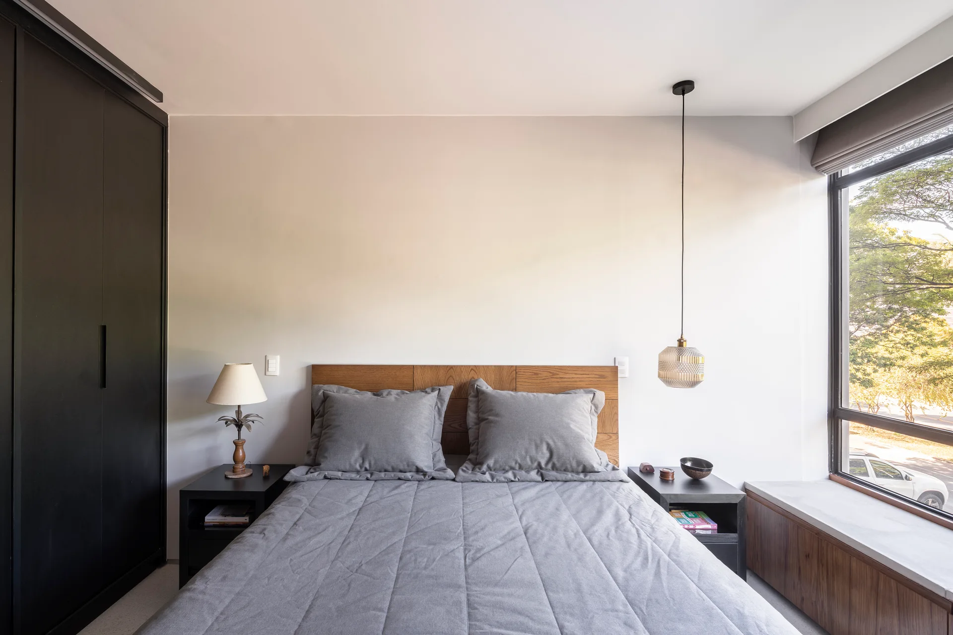 A contemporary bedroom featuring a gray quilted bed, a wood headboard, a large black built-in wardrobe, and a built-in window seat.