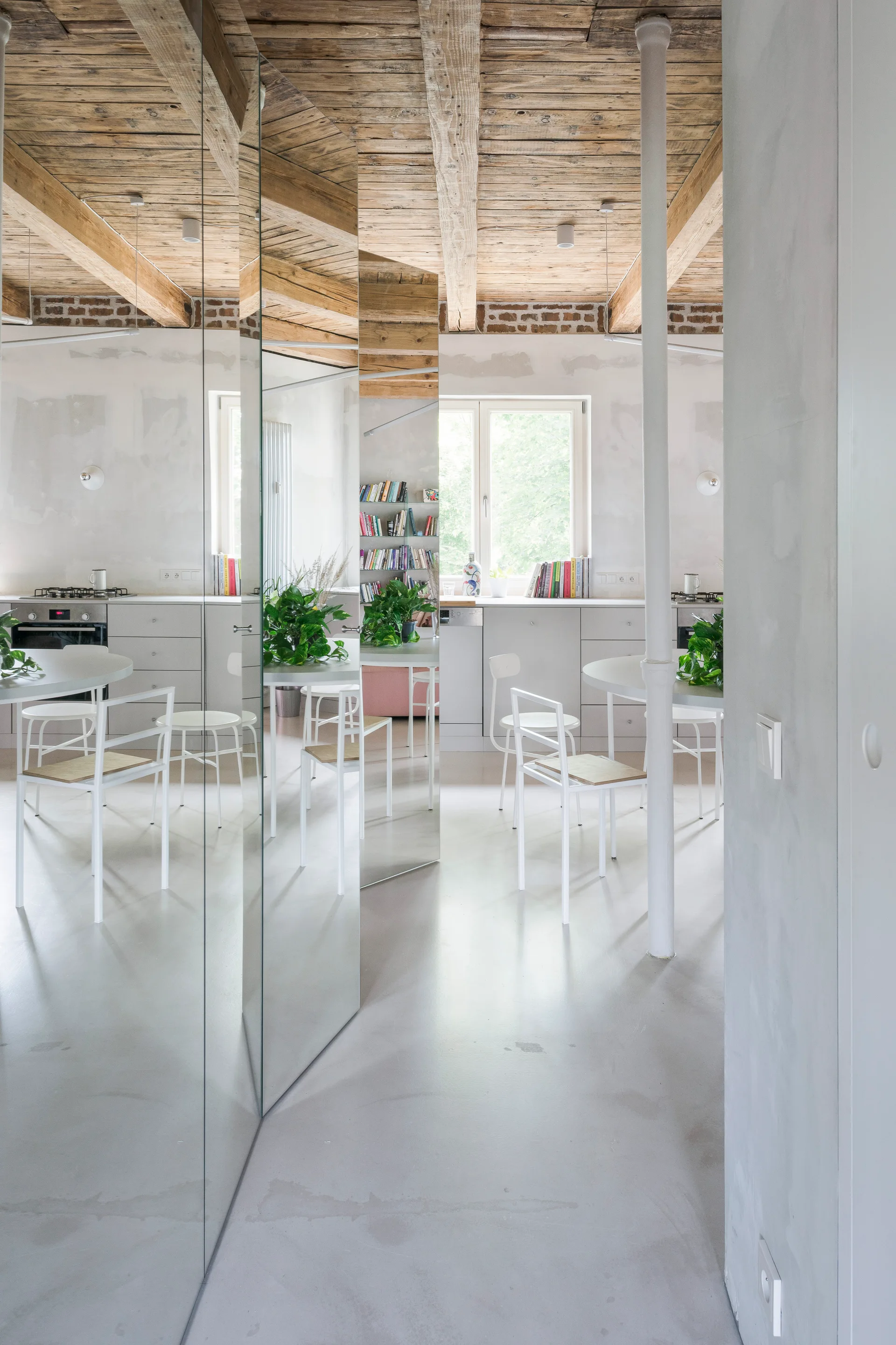 A modern dining area featuring a faceted mirrored partition wall, white dining chairs and table, and a rustic exposed wood plank ceiling.
