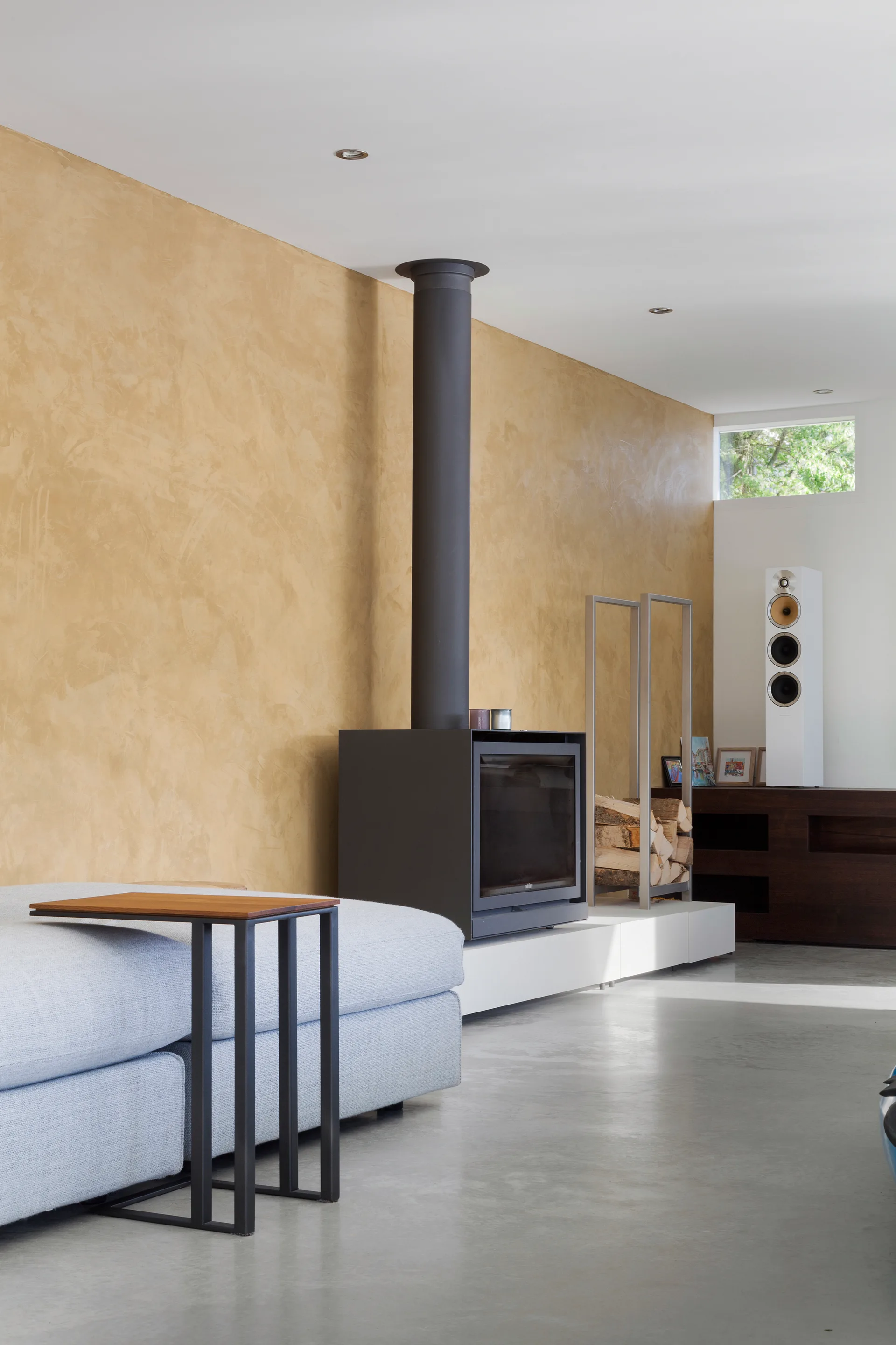 A modern living space featuring a textured gold plaster wall, a minimalist black fireplace on a white platform, and a grey sofa.
