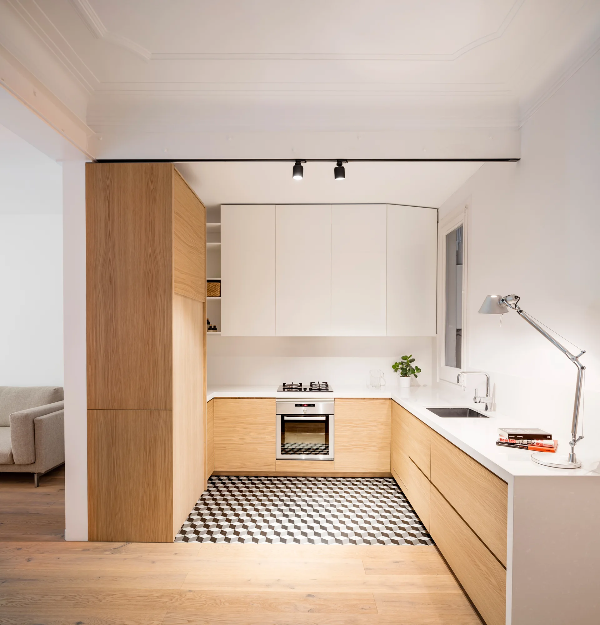 A modern U-shaped kitchen with light wood lower cabinets, white upper cabinets, and black and white geometric patterned floor tiles.