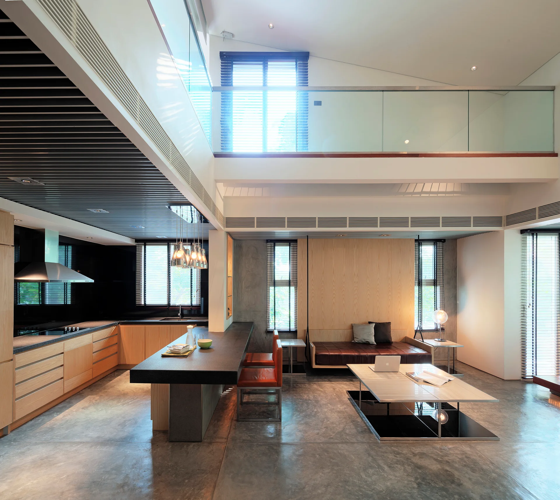A modern open-plan interior showing a kitchen with a dark stone island next to a living area with a leather daybed on a concrete floor.