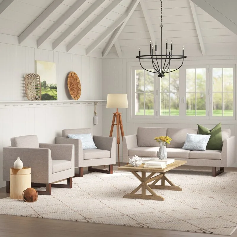 A bright farmhouse living room with neutral upholstered seating, a rustic wood coffee table, and a black metal chandelier under a vaulted ceiling.