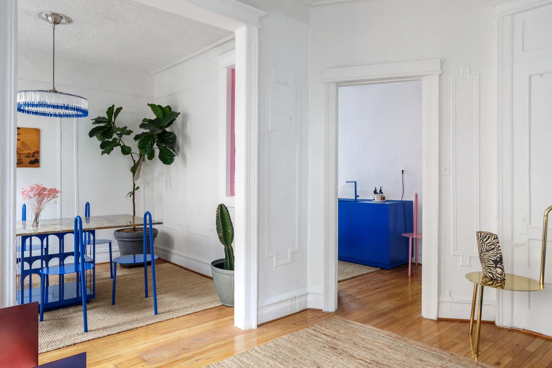 Cobalt blue metal dining chairs and table sit on a sisal rug in a white dining room with wall moldings.