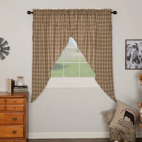 Brown and beige plaid swag curtains hang over a window next to a wooden dresser and a rustic wicker basket holding a decorative pillow.