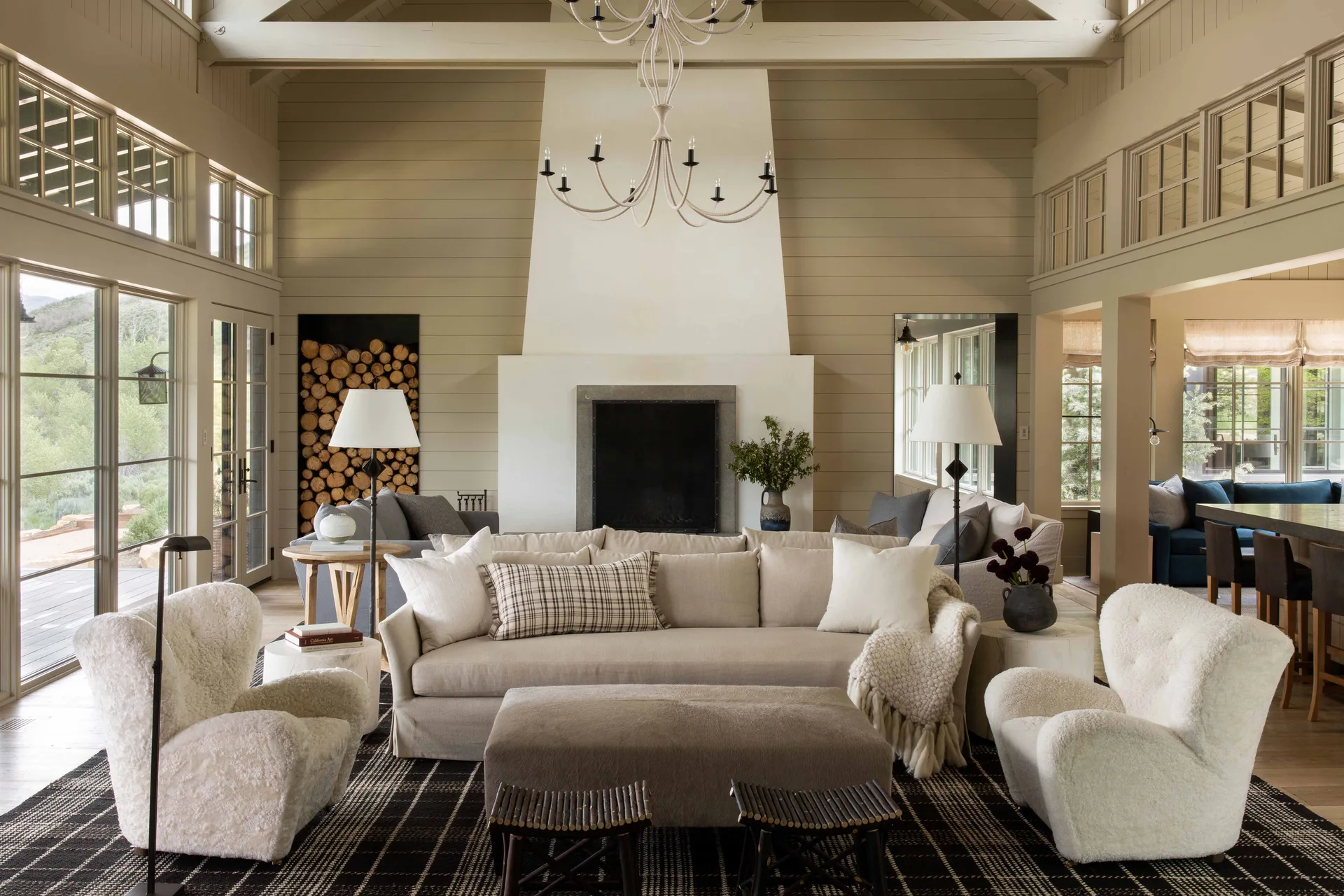A spacious living room with a large white fireplace, a neutral sofa, two fuzzy white armchairs, and a built-in firewood alcove.