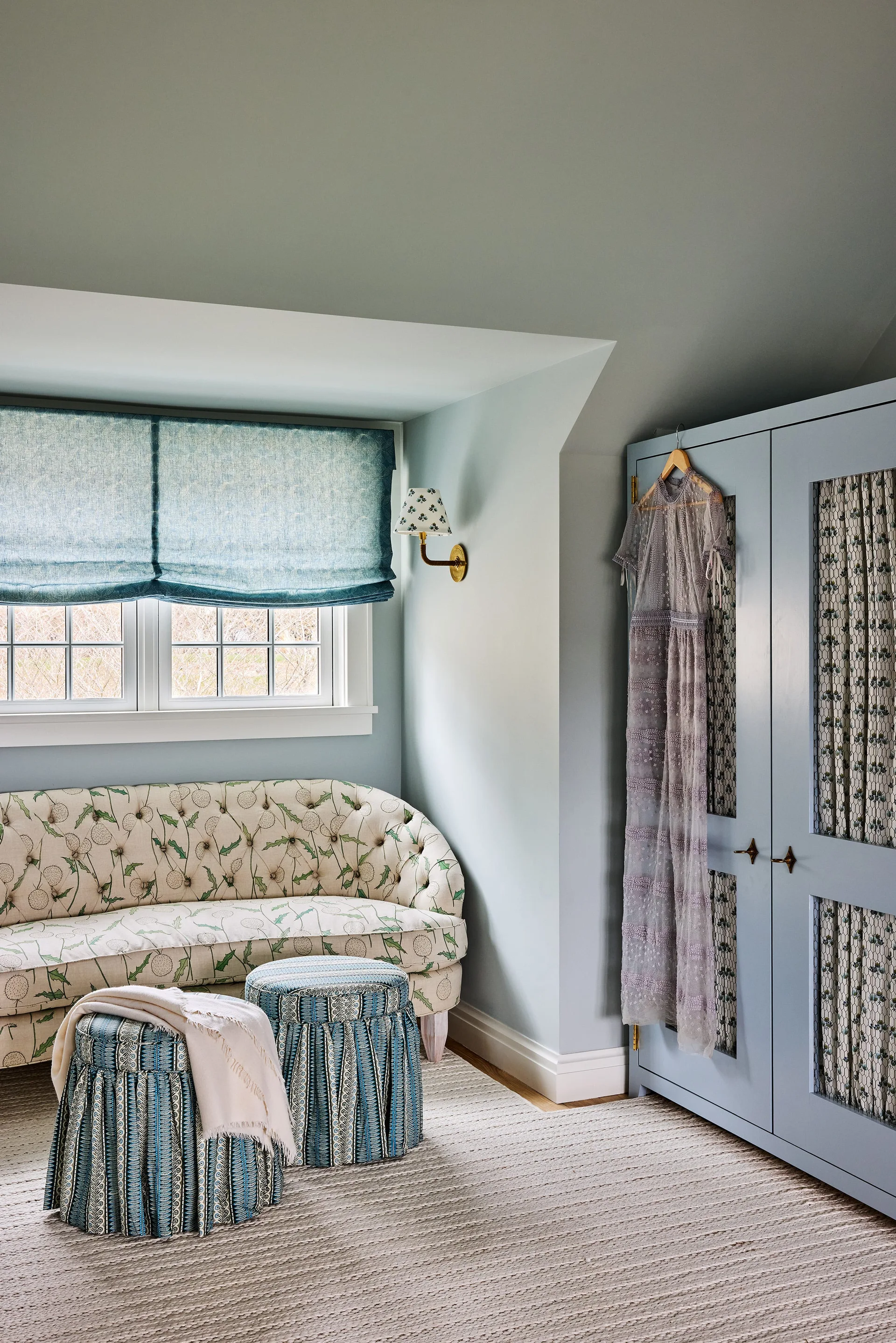 A light blue bedroom corner features a tufted floral sofa, two striped fabric stools, and a built-in wardrobe with mesh panels.