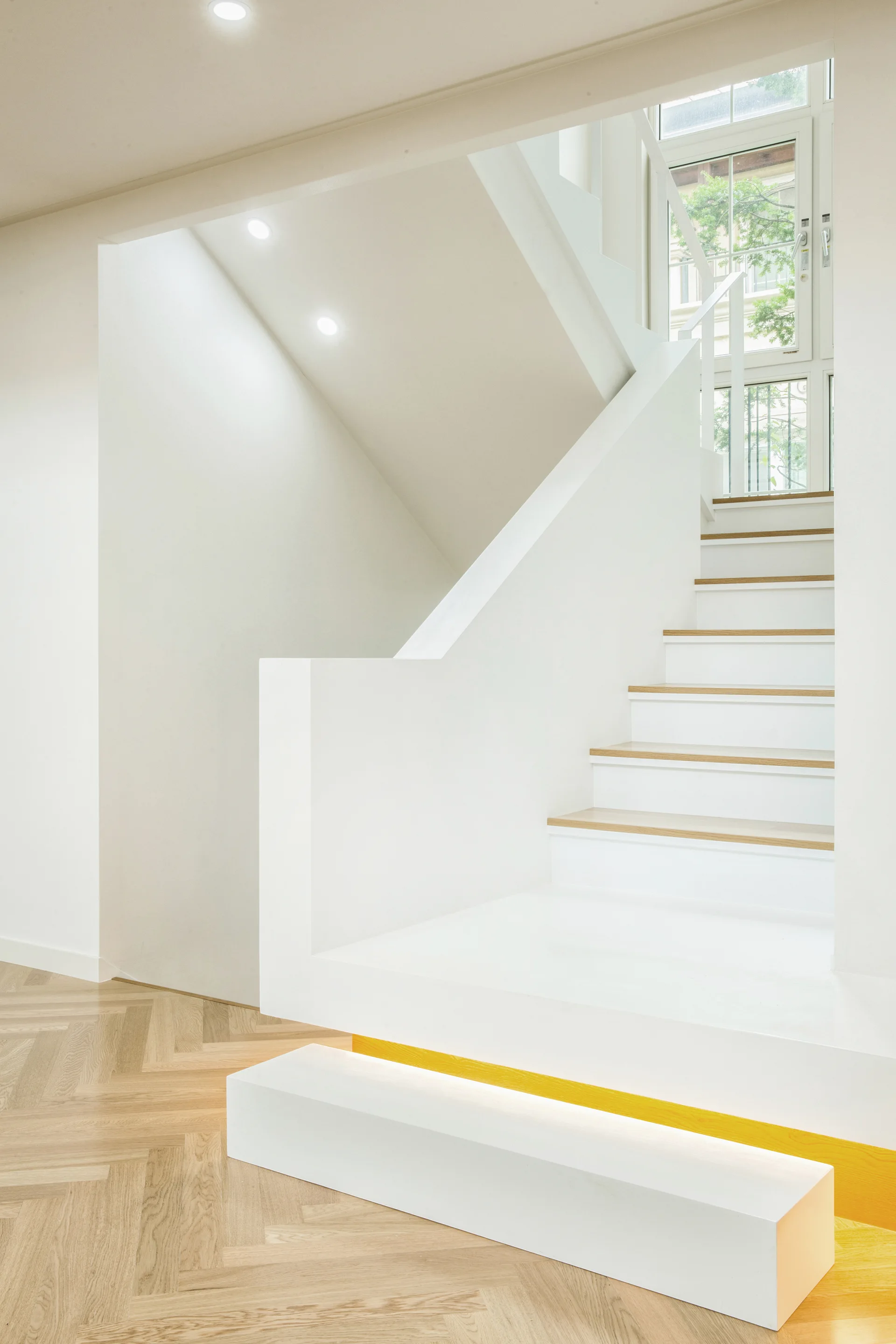 A minimalist white staircase with light wood treads, integrated under-step lighting, and a light wood herringbone floor.
