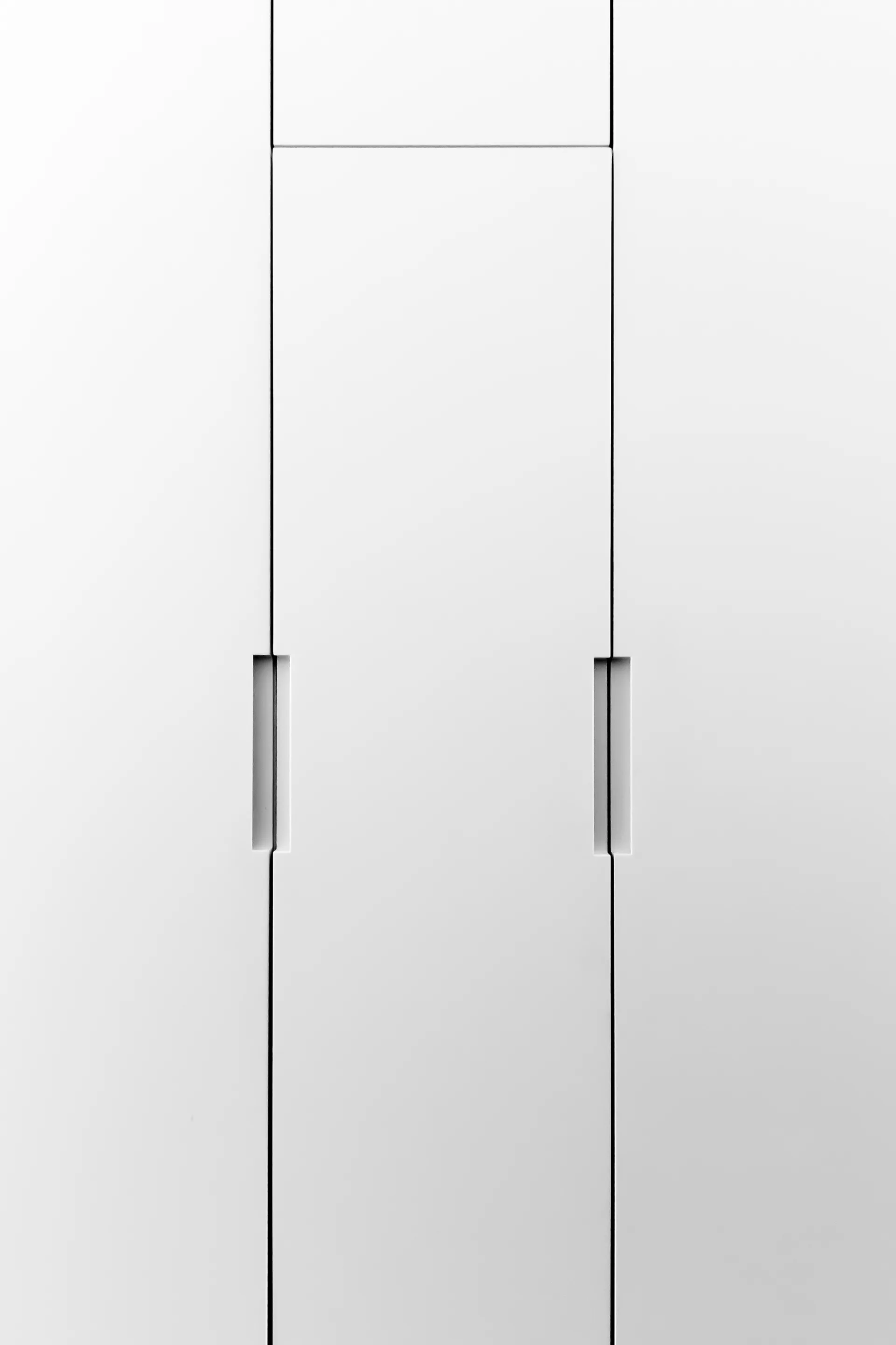 Close-up of flat-panel matte white cabinet doors featuring recessed vertical integrated handles with clean vertical seams.