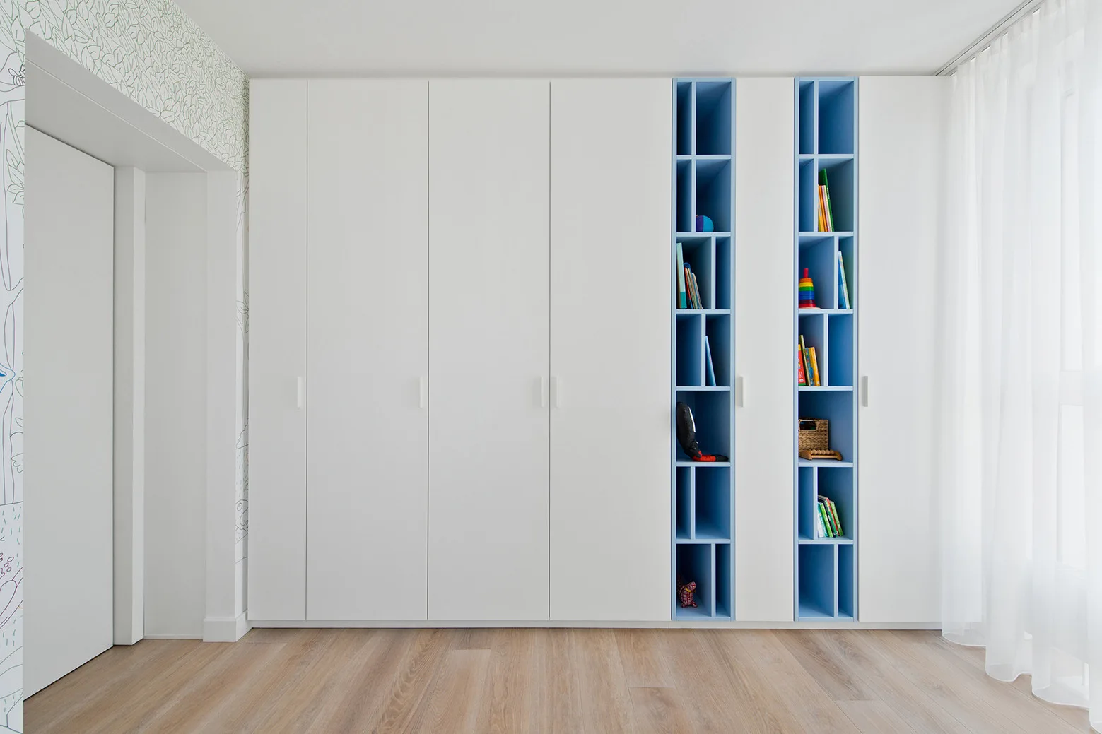 A large built-in white wardrobe features two vertical columns of light blue open shelving holding books and toys.