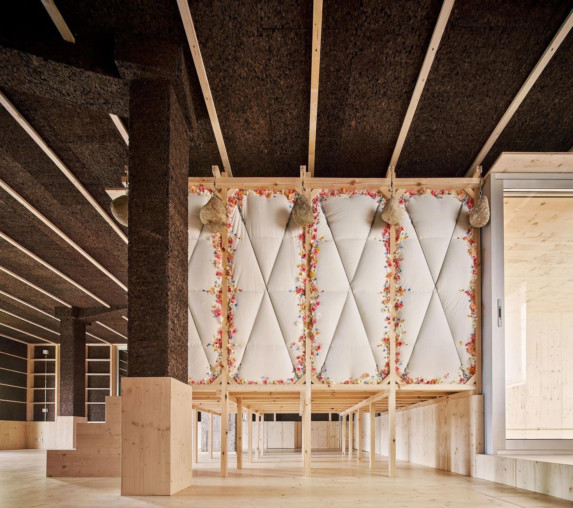 An architectural interior featuring a dark textured cork ceiling with exposed wood beams and a white cushioned partition wall framed in timber.