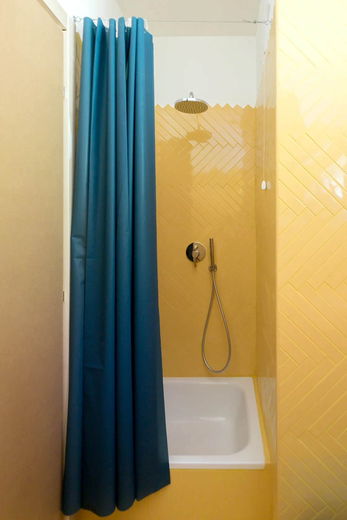 A bathroom shower featuring bright yellow herringbone tiled walls, a white tub, chrome fixtures, and a teal shower curtain.