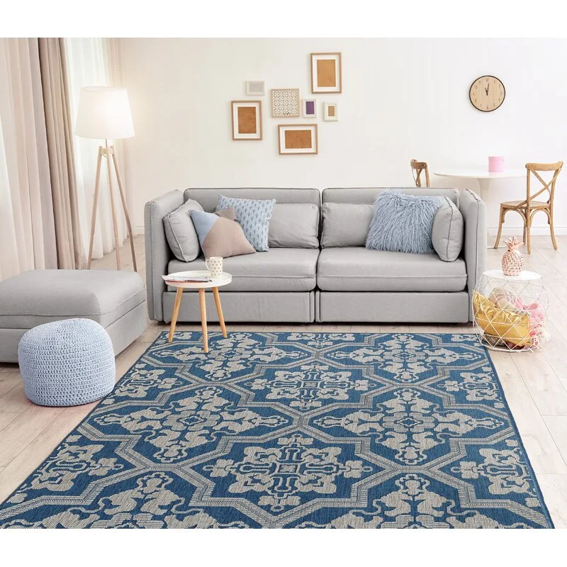 A Scandinavian living room featuring a gray sofa, a large blue patterned area rug, a tripod floor lamp, and a small wooden side table.