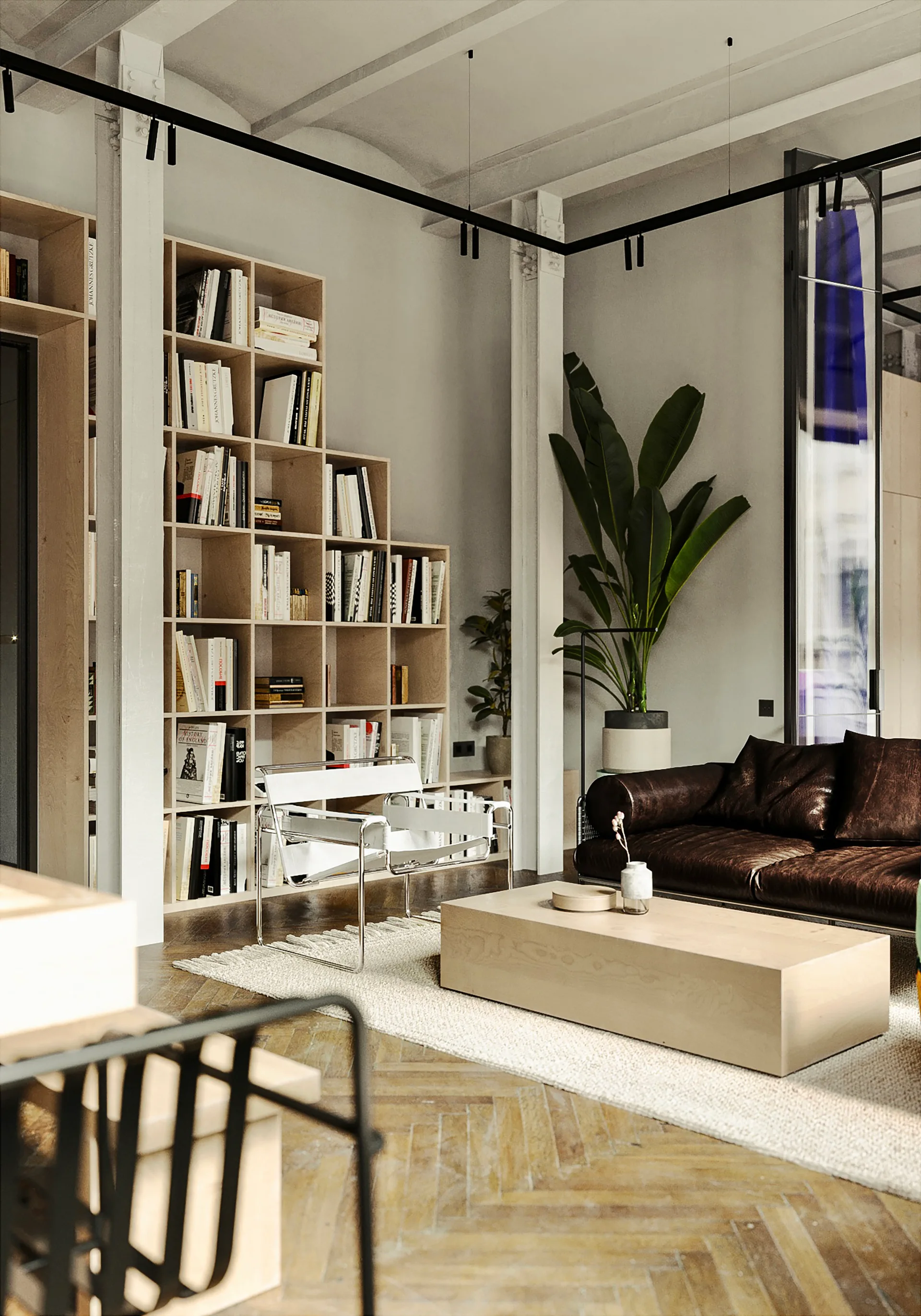 A minimalist living room features a dark leather sofa, a low wooden coffee table, a white sling chair, and a large light-wood grid bookshelf.