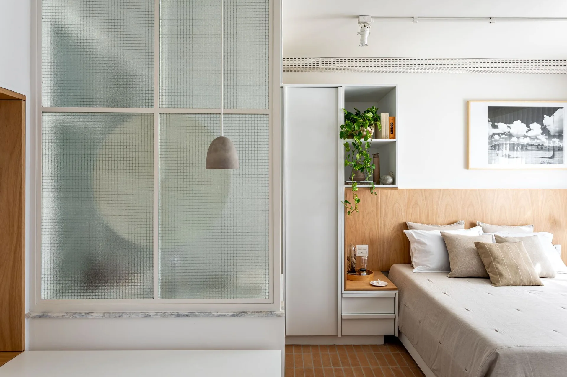 A modern bedroom featuring a wood-paneled headboard wall, built-in white cabinets with open shelving, and a metal-framed textured glass partition wall.