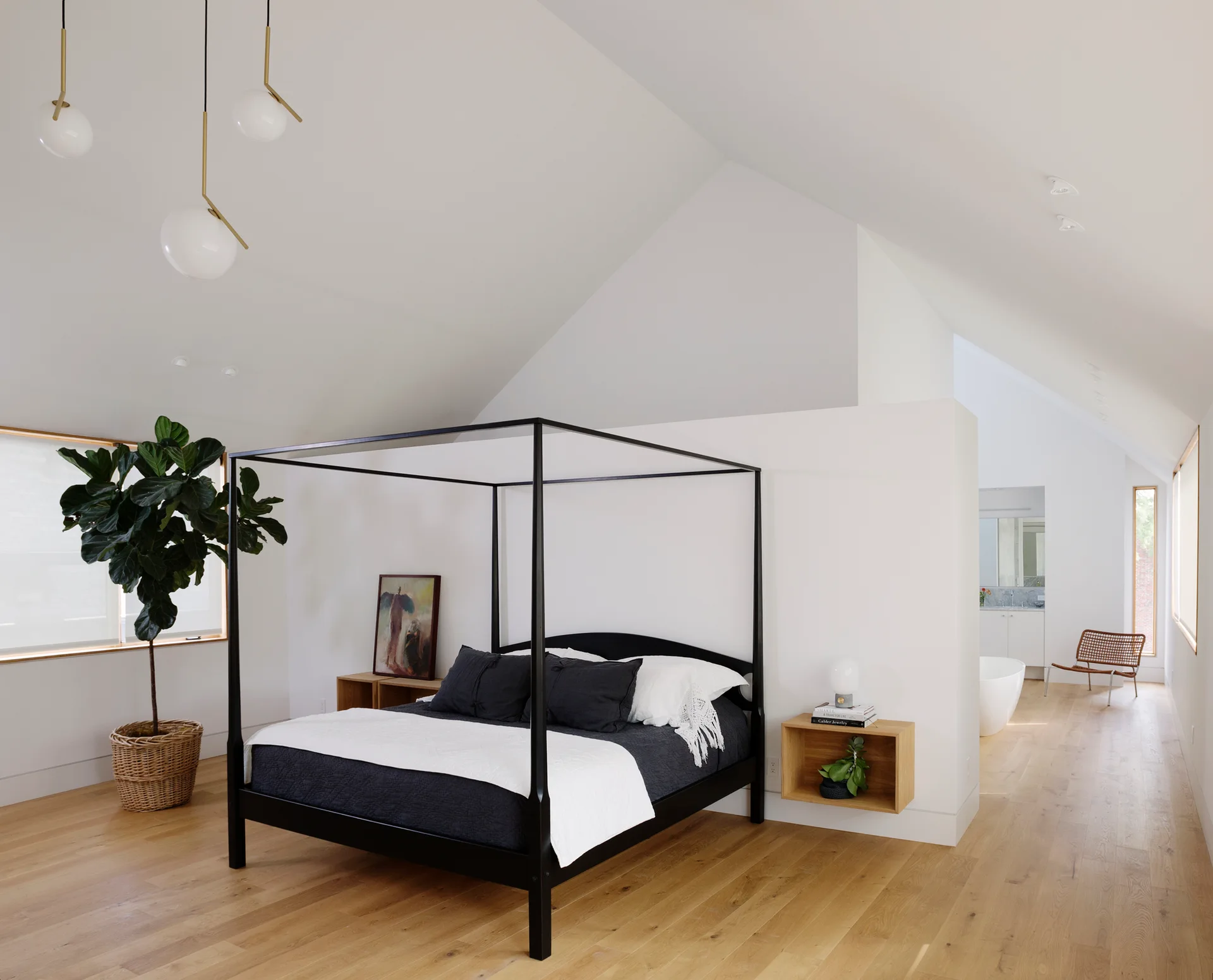 A minimalist white bedroom featuring a black canopy bed, light wood floors, a vaulted ceiling, and a partition wall dividing the bath area.