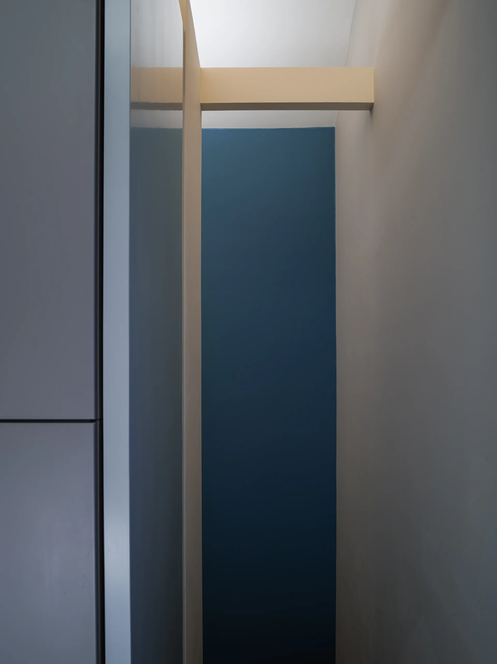 A minimalist architectural nook featuring a deep blue painted wall, a light neutral structural beam, and a smooth grey cabinet panel.