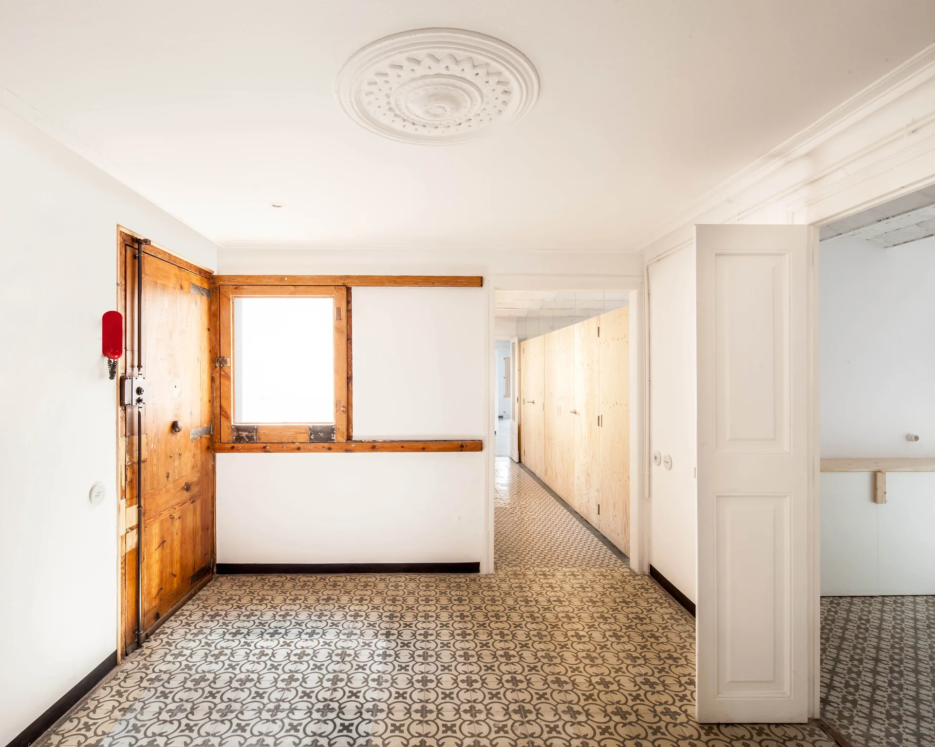 An entryway features a patterned gray and white tile floor, a rustic wood entry door, a small wood-framed window, and an ornate white ceiling medallion.