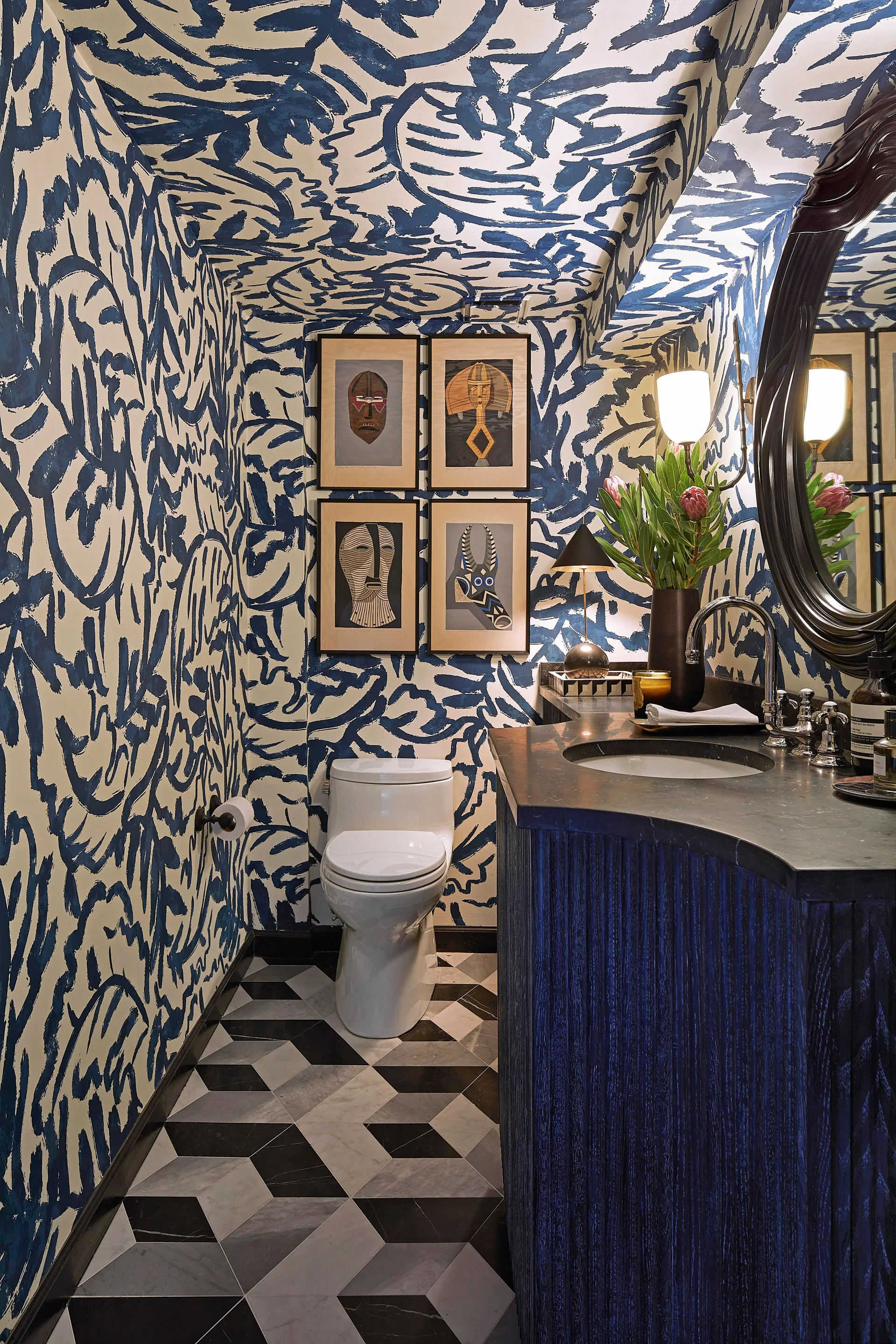 A bold powder room featuring blue and white patterned wallpaper on the walls and ceiling, a dark fluted vanity, and geometric marble floor tile.